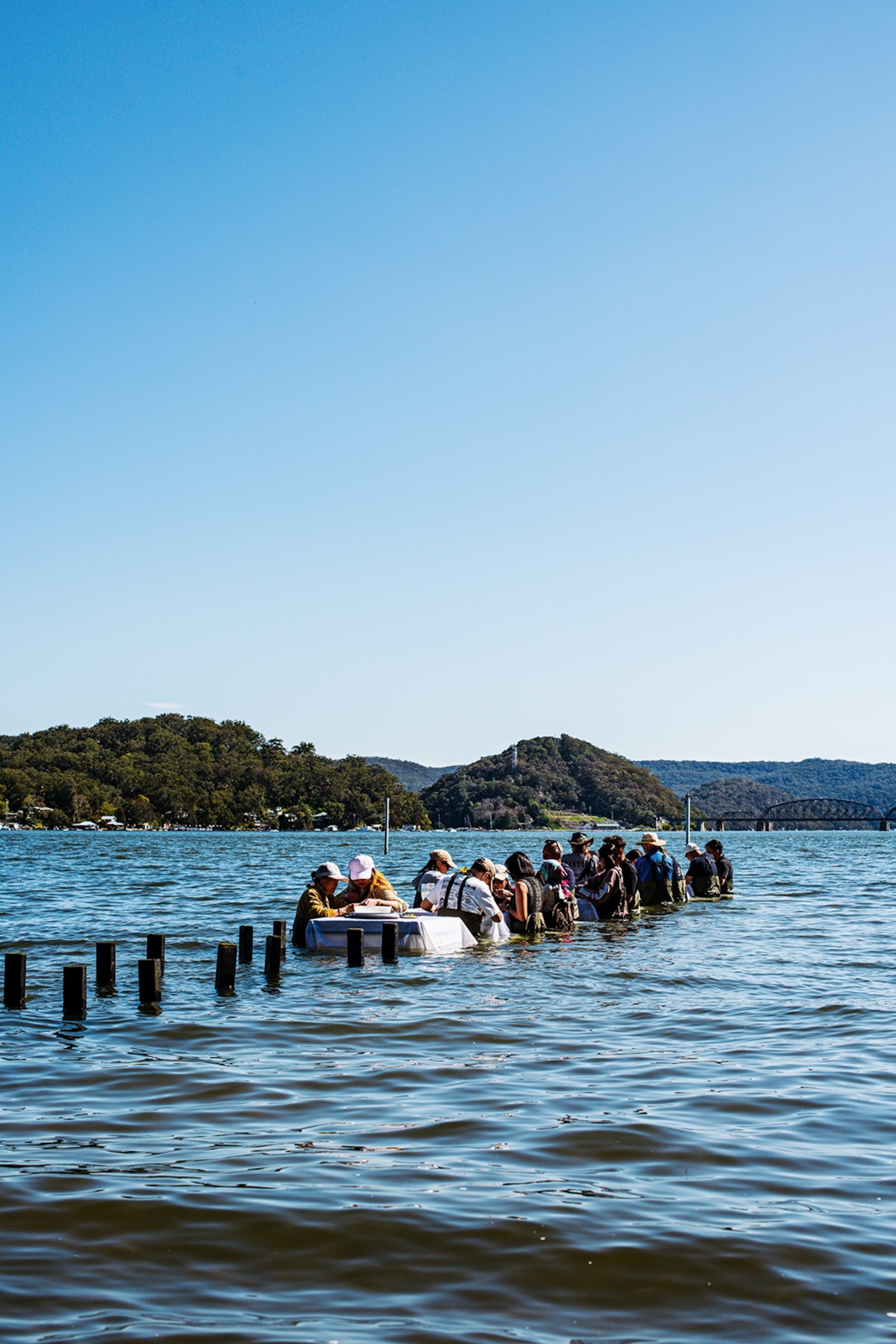 A long table half-submerged in a bay with guests standing around it.