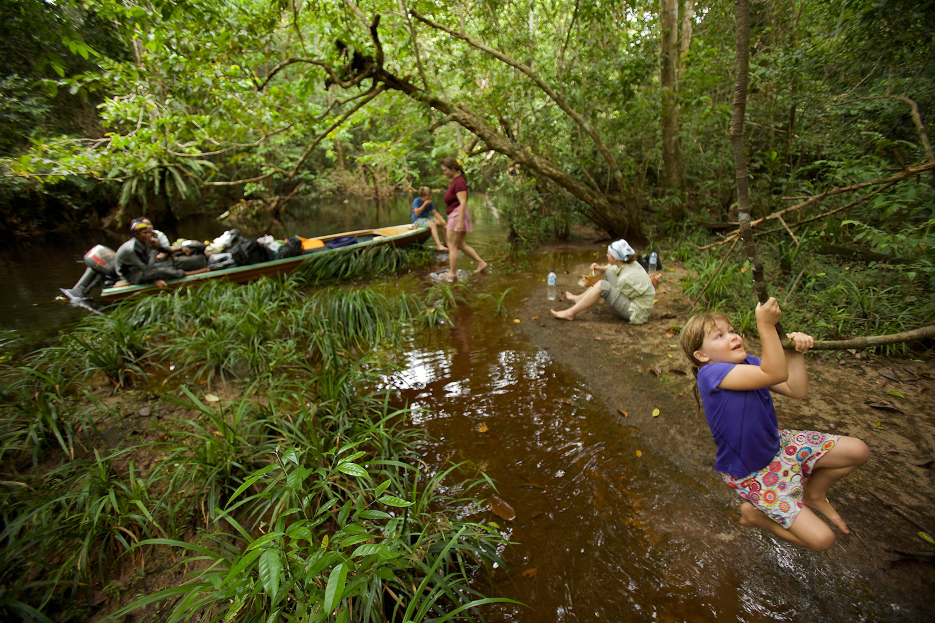 A rest stop along the river on the boat trip up to Cabang Panti Research Site, Gunung Palung. Jessica swings on a vine. 2010