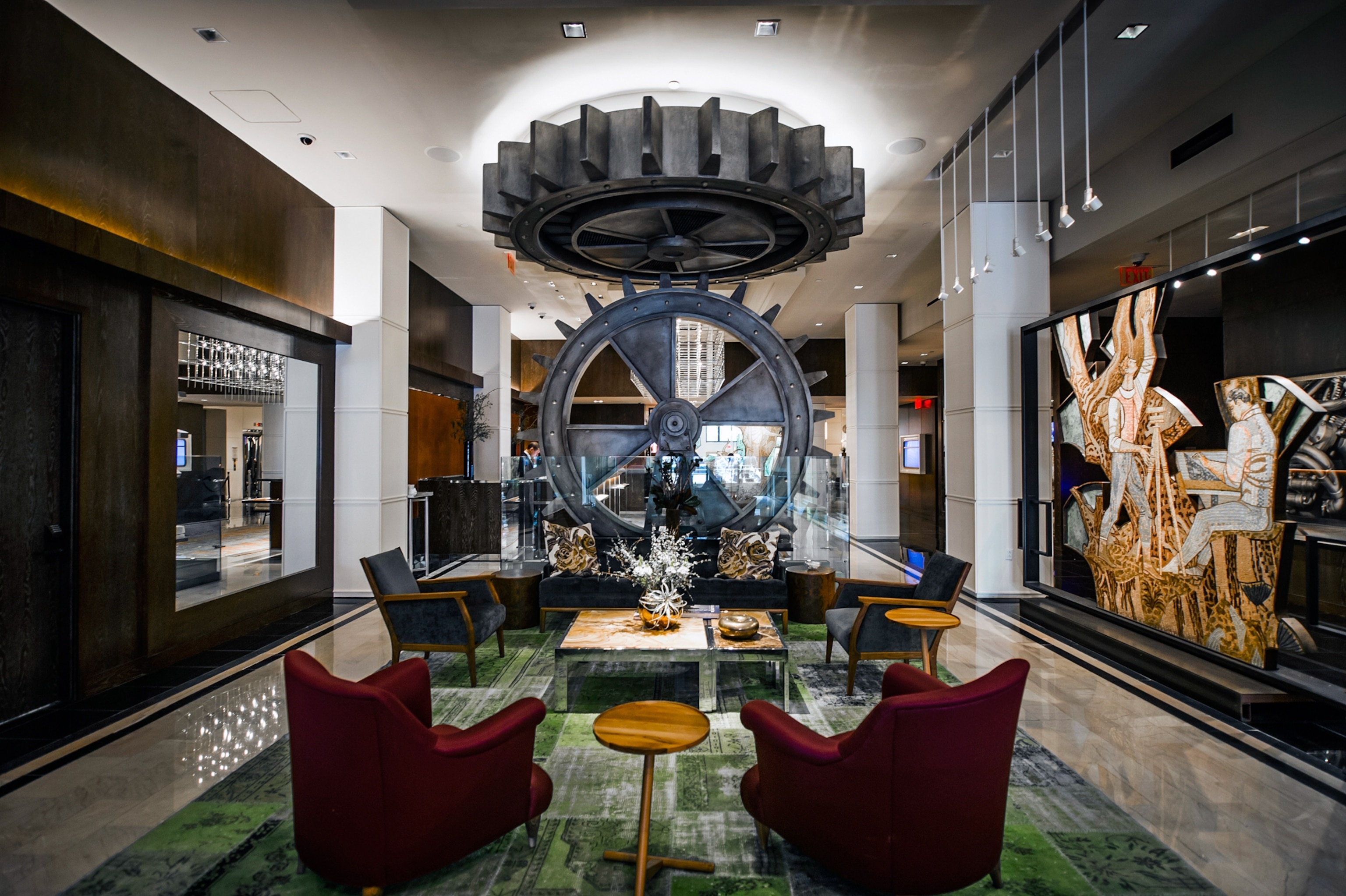 An interior of a hotle has chairs soft carpet and artistic decor.