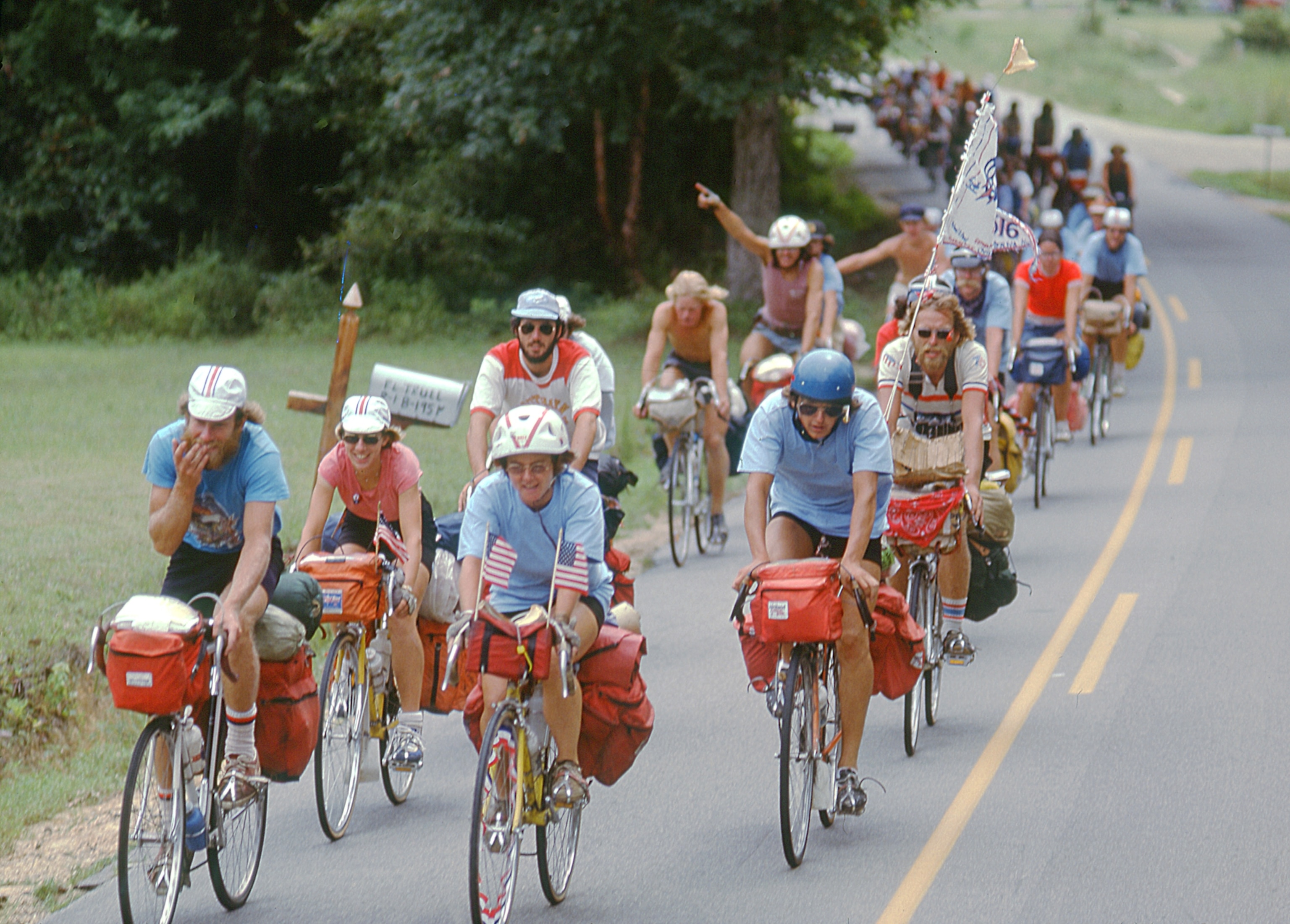 A group of bicyclists wearing red, white, and blue ride down an asphalt road.