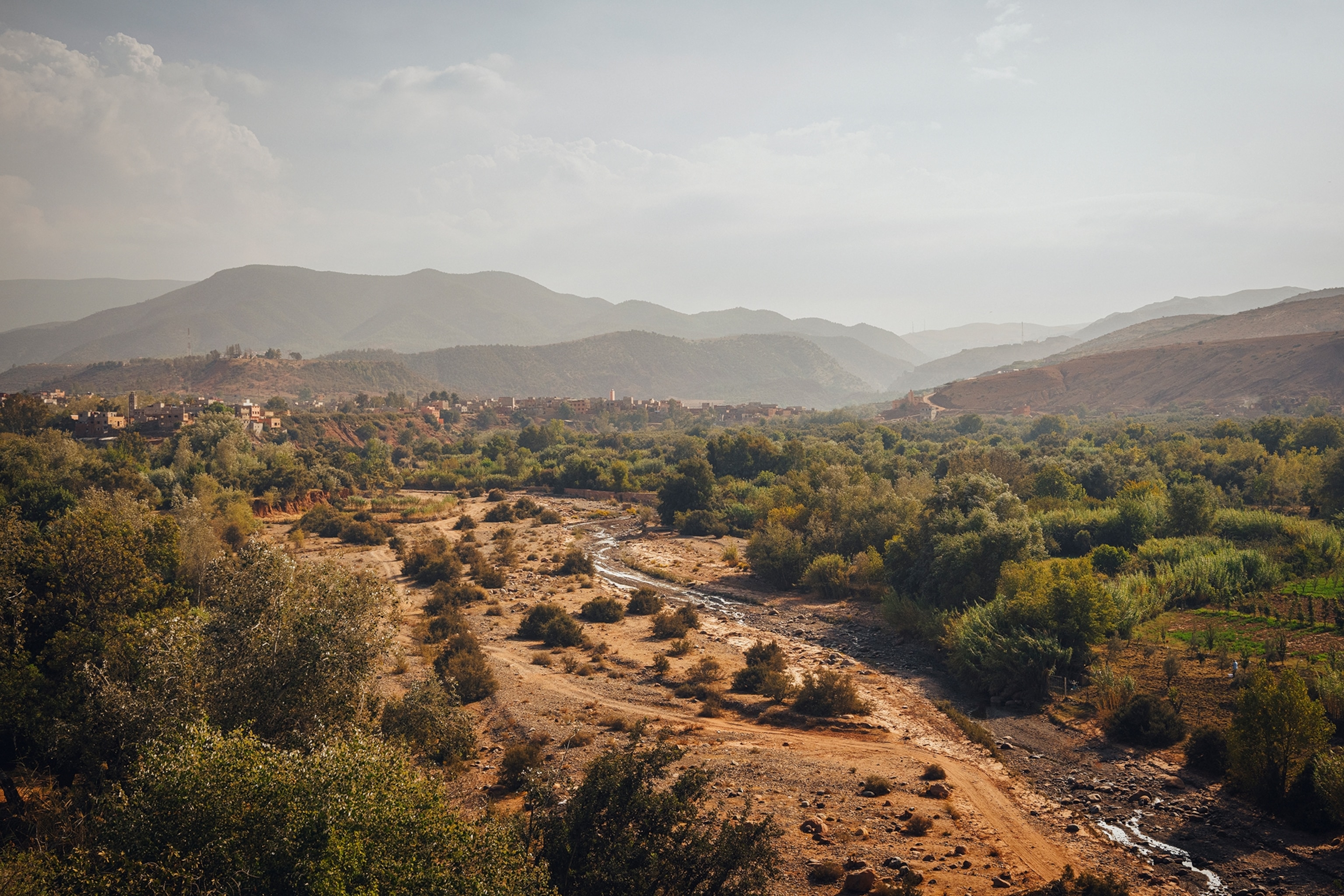 A landscape shot of an arid, low-reaching mountain valley with a small river running towards a small city in the distance.