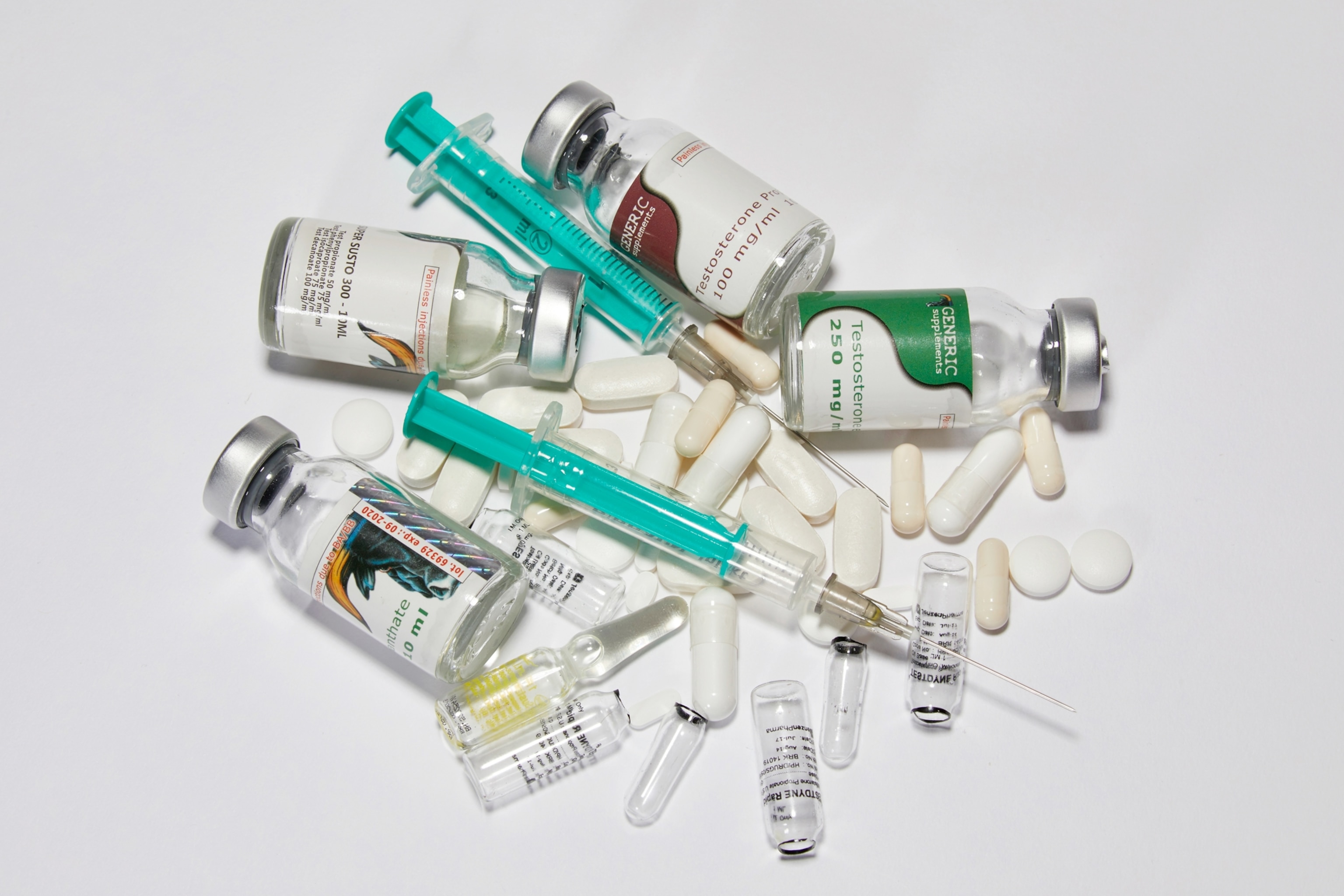 A collection of medicine vials, syringes, capsules, and tablets scattered on a white surface
