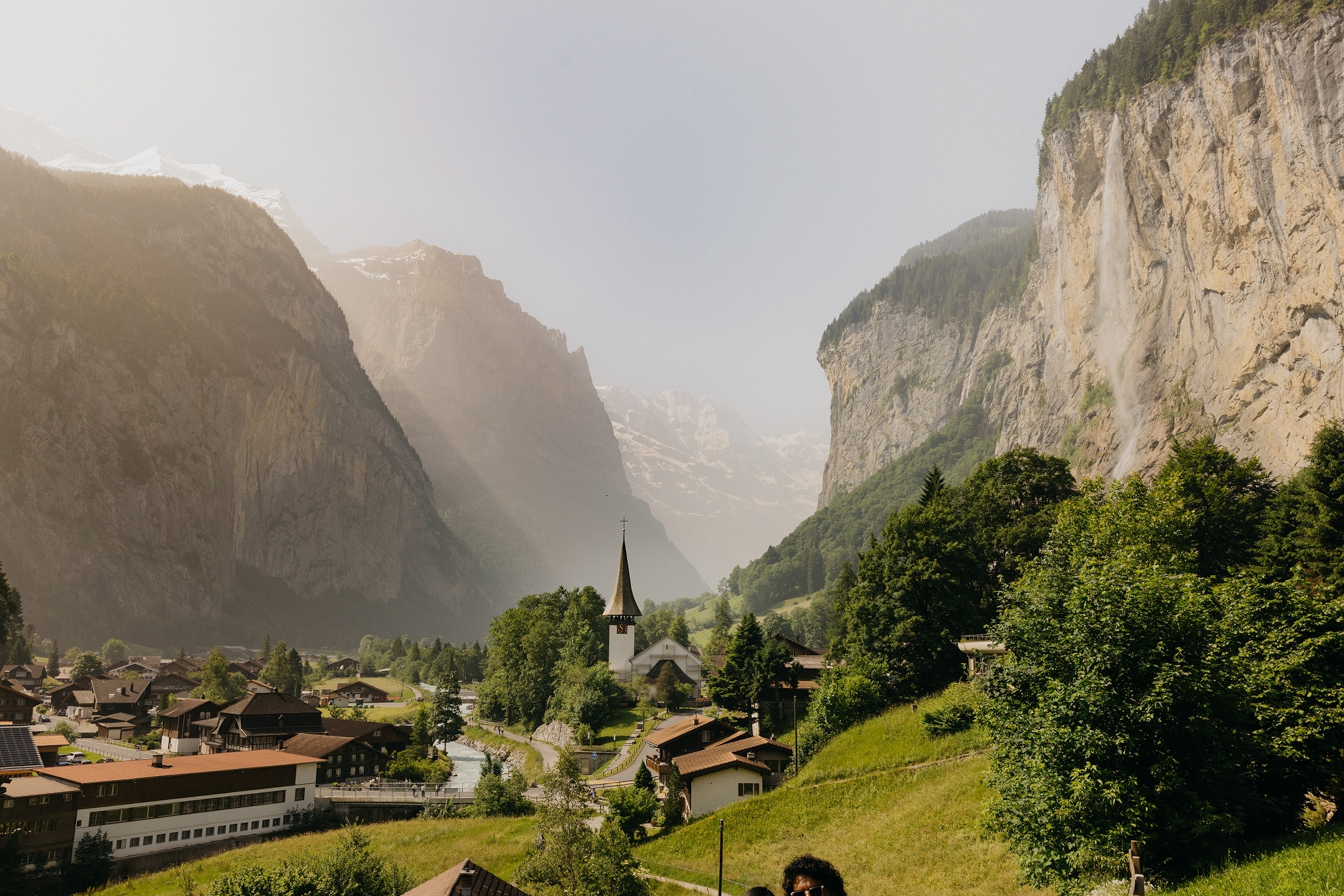 A mountain valley with mist settled in between the mountains and a village in a green valley.