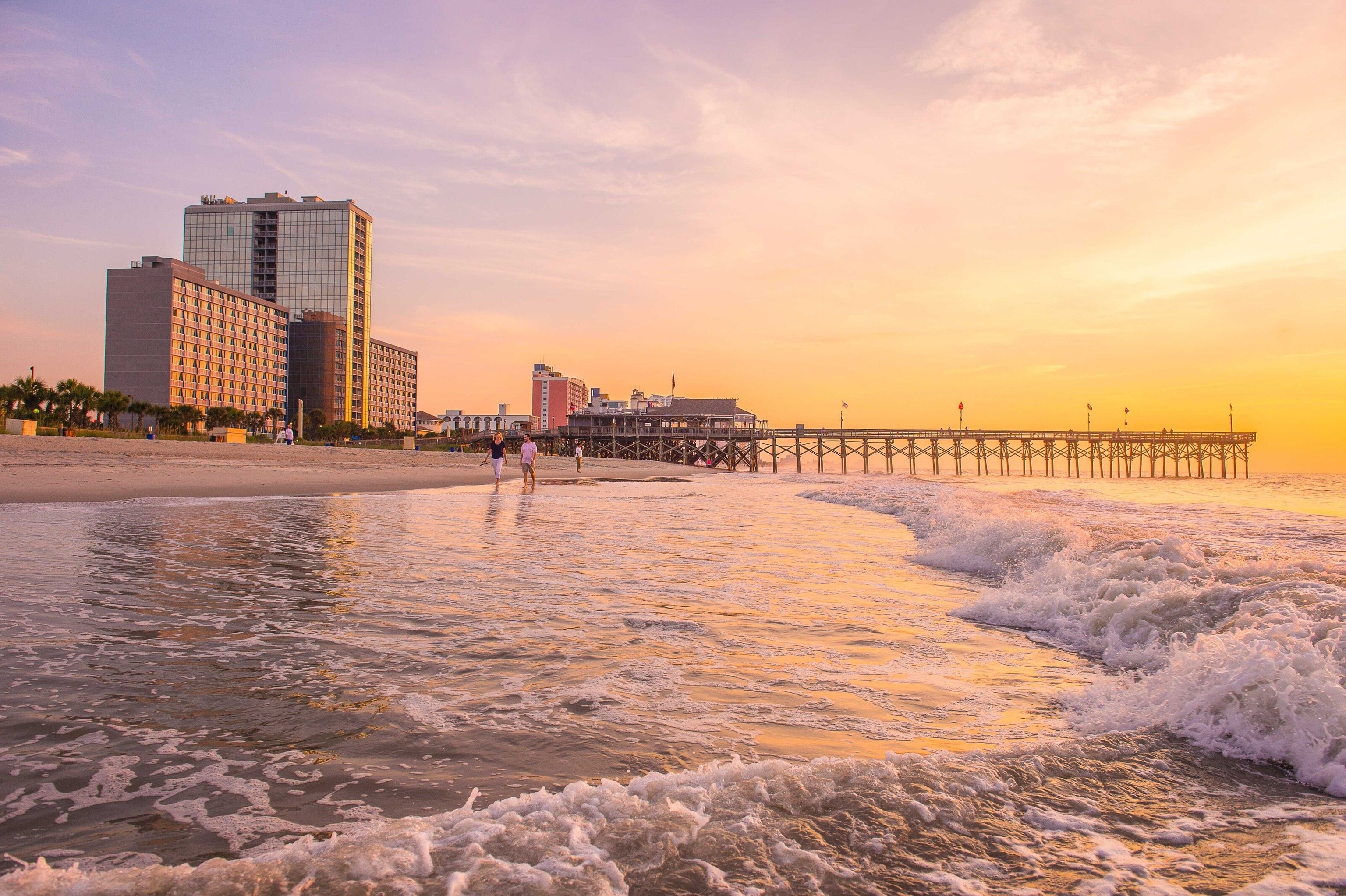 Waves break on Myrtle Beach at sunset. A pier stretches out to sea in the background.