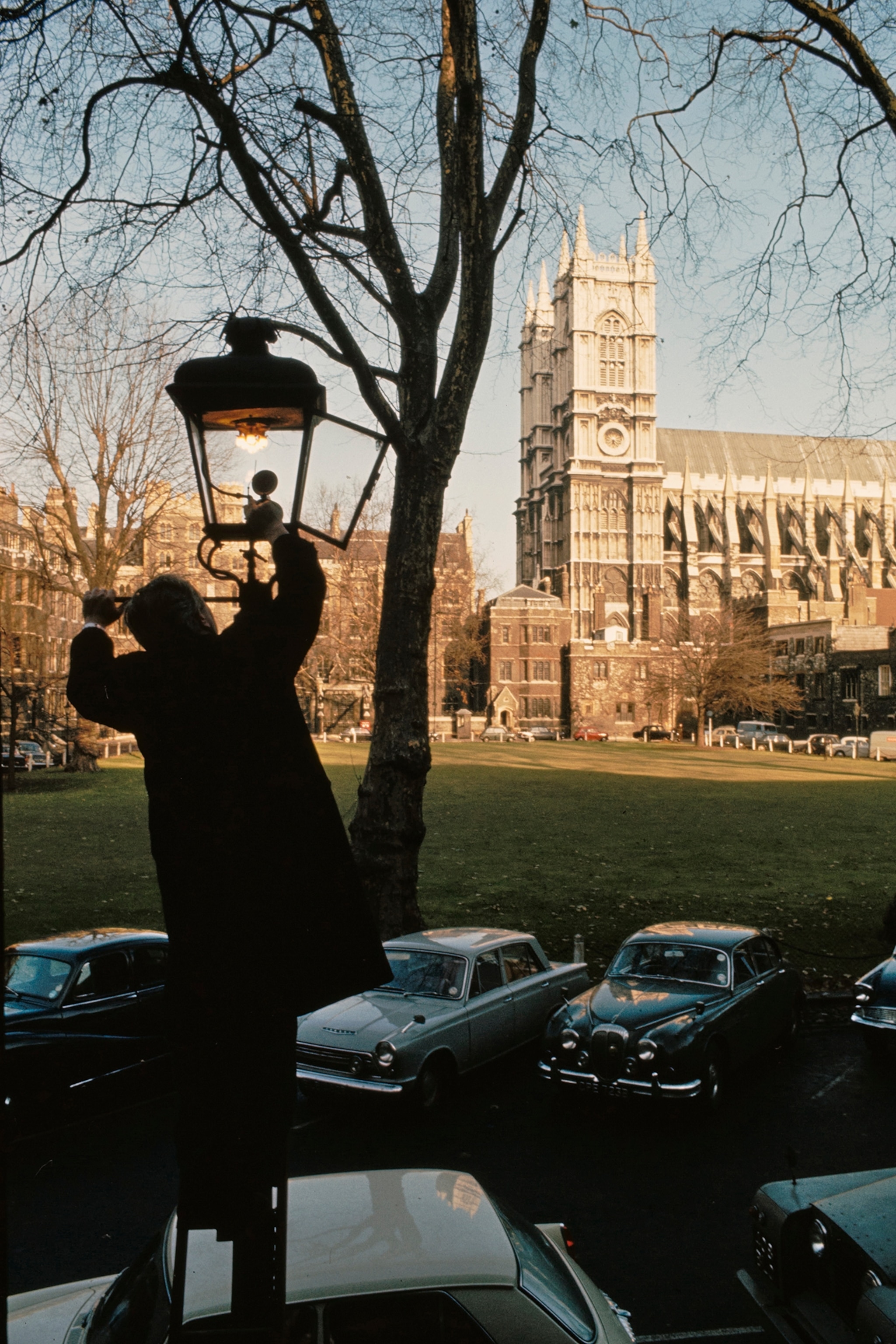 Westminster Abbey framed by silhouette of man lighting a street lamp.