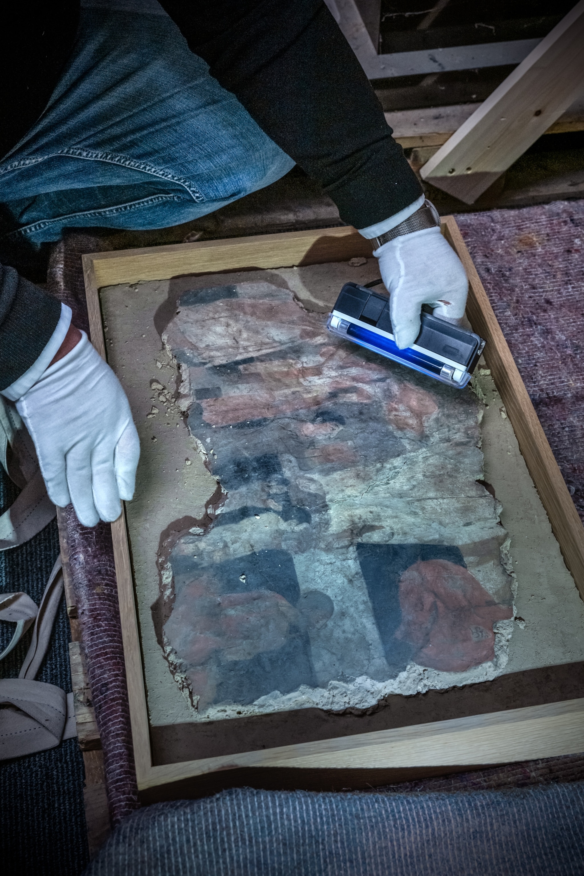 Glove hands scan a fresco in a box.