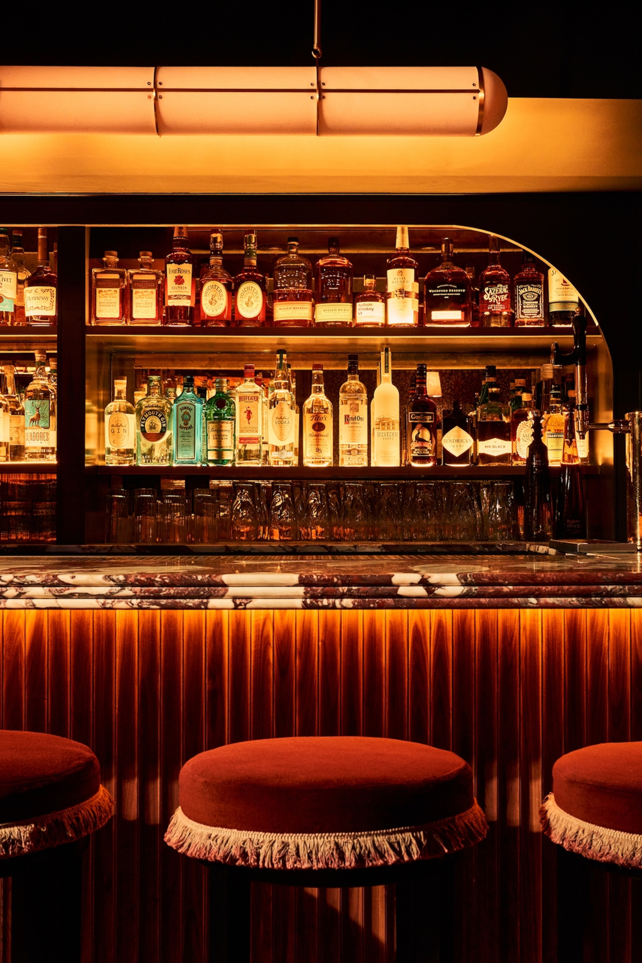 A back-lit bar with velvet-padded stools and bottles of liquor lining the shelves at Mulberry in New York City.