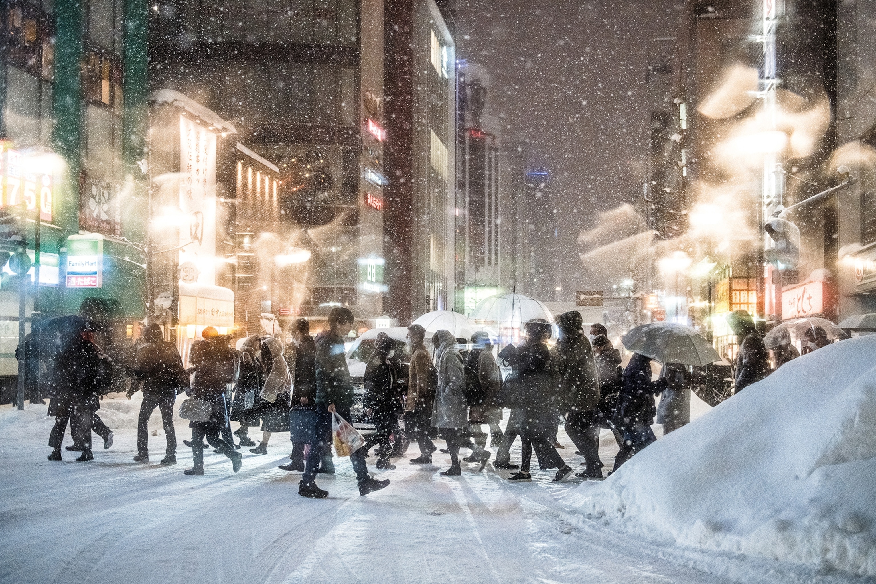 A busy crossing in a high-rising city at snowfall with warmly wrapped up locals streaming across the street.