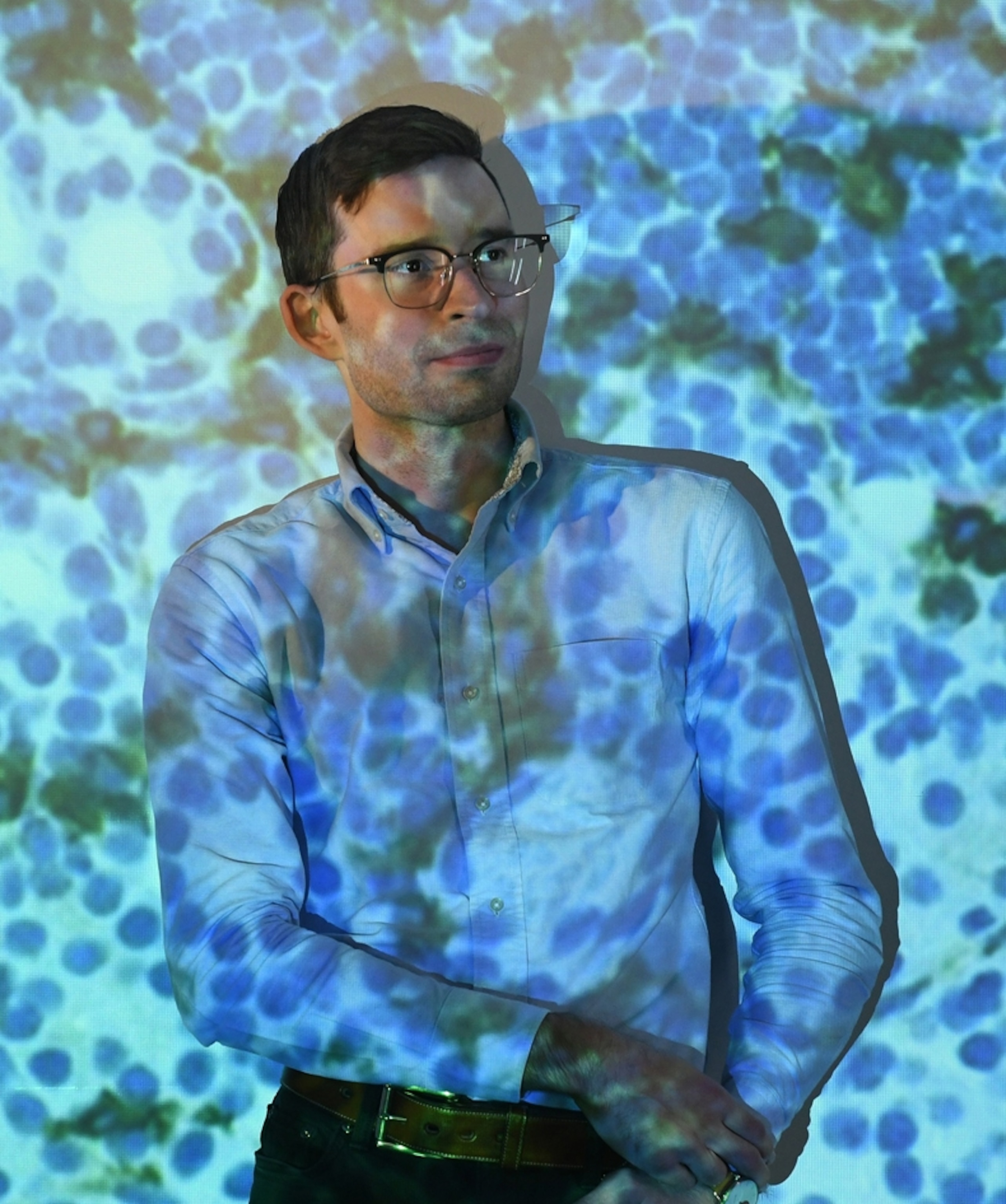 A man stands for a portrait in front of projected blue shapes