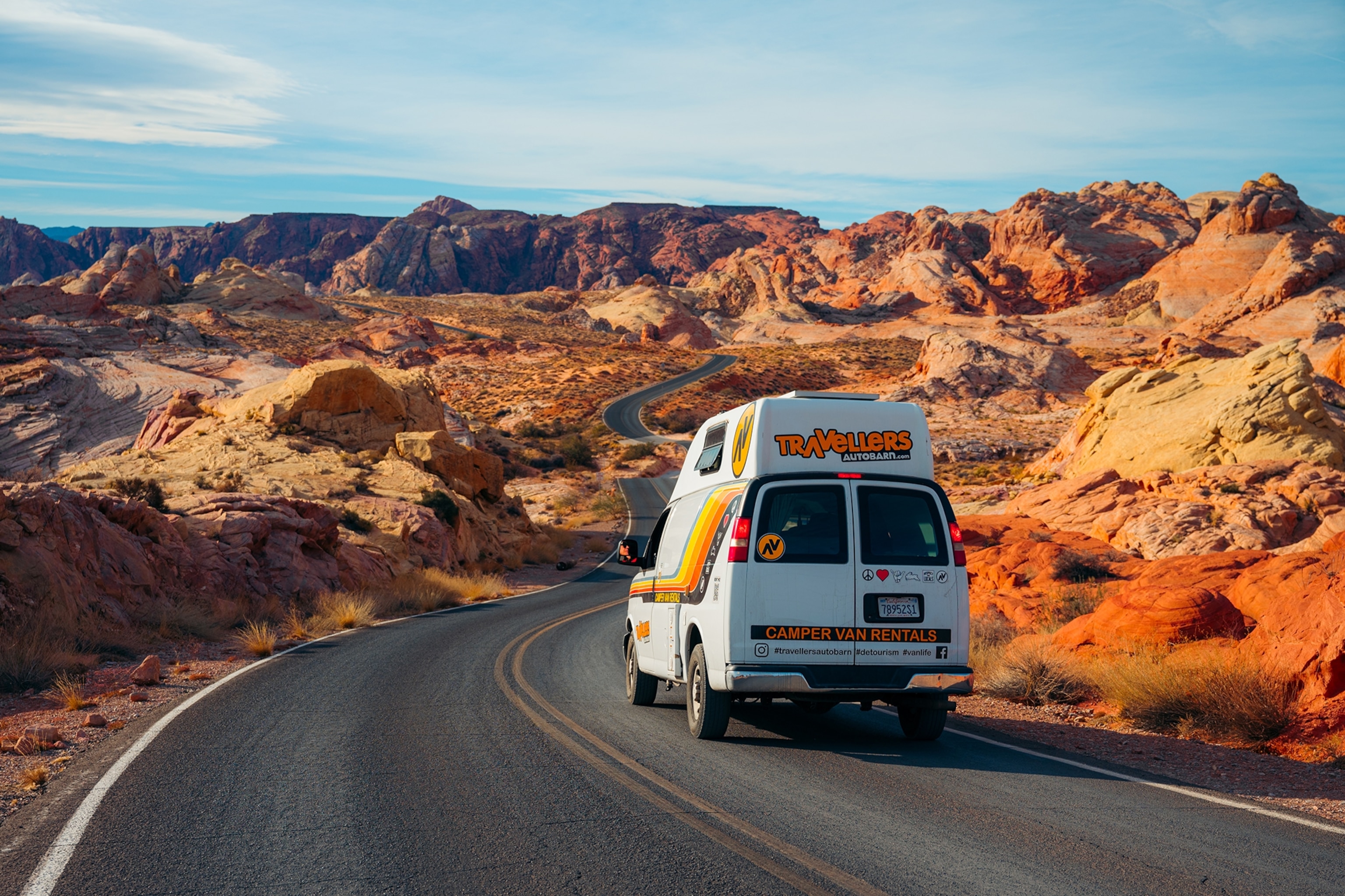 Campervan driving along a road surrounded by red, rocky terrain


