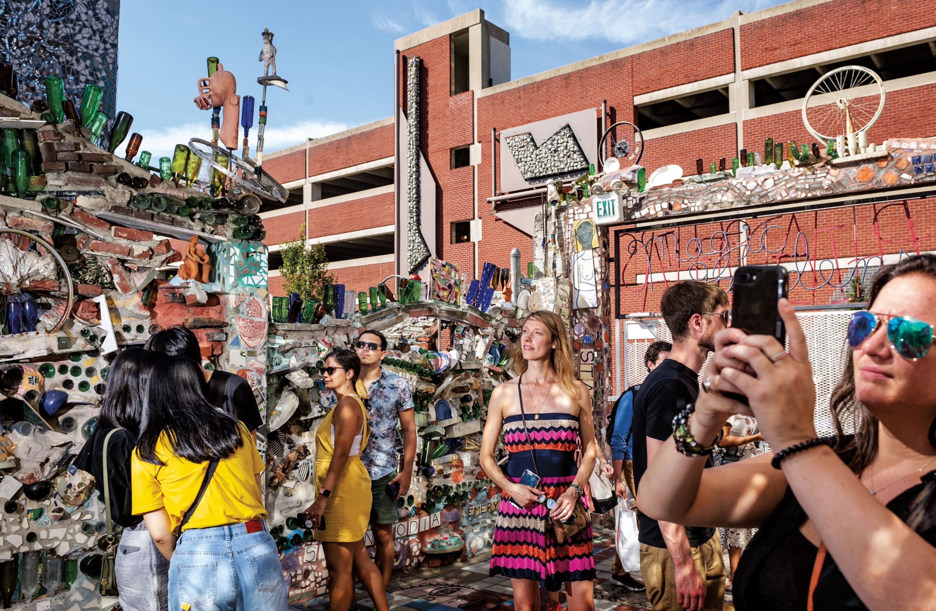 People take pictures of and walk through an outdoor art exhibition created in a garden.