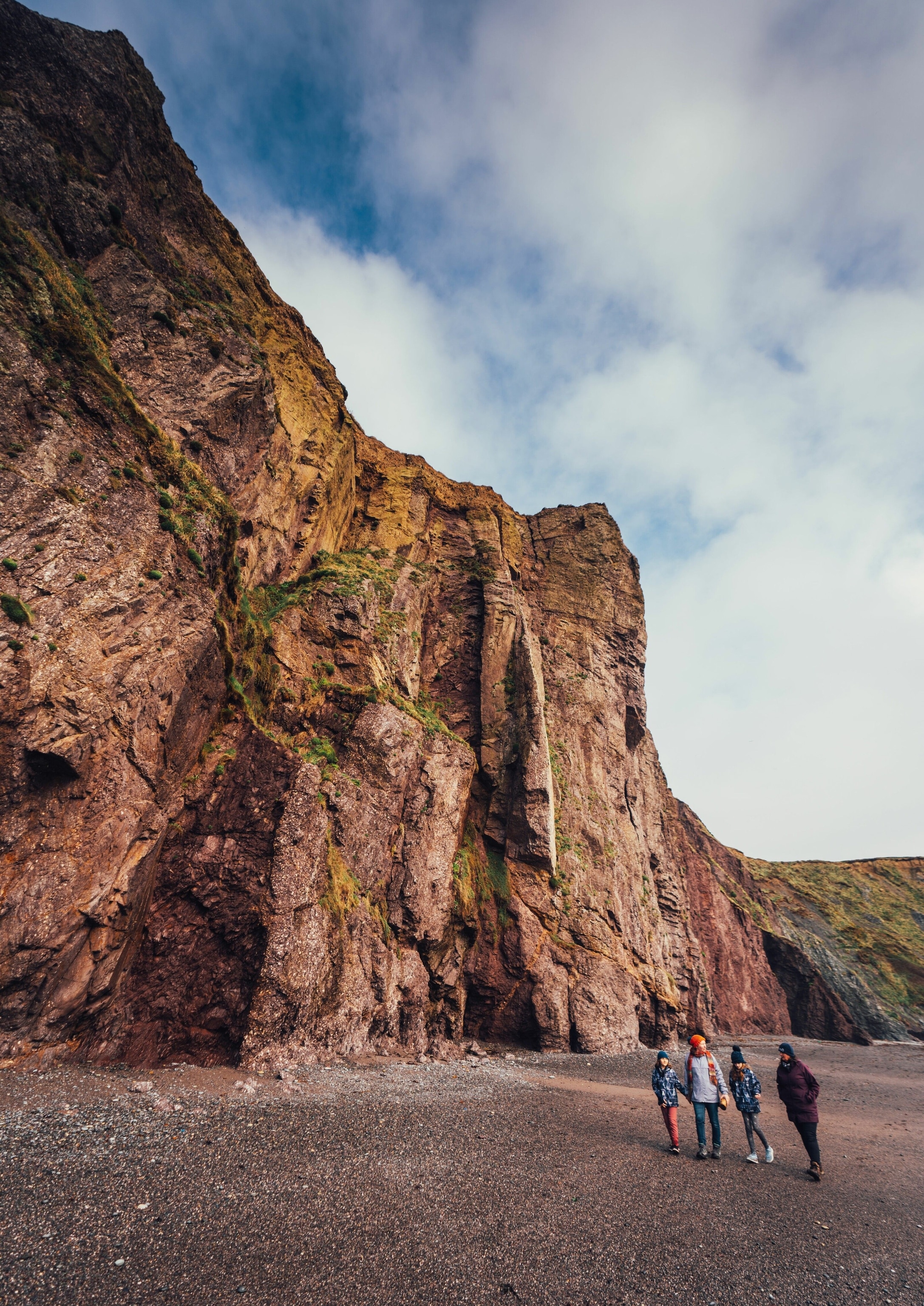 People walk on a beach past a cliff.