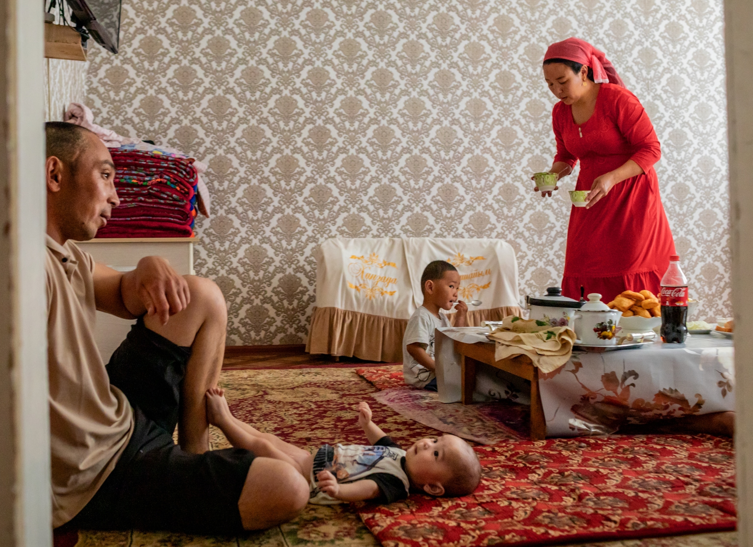 A woman prepares lunch at her home, as her husband watches over their sons.