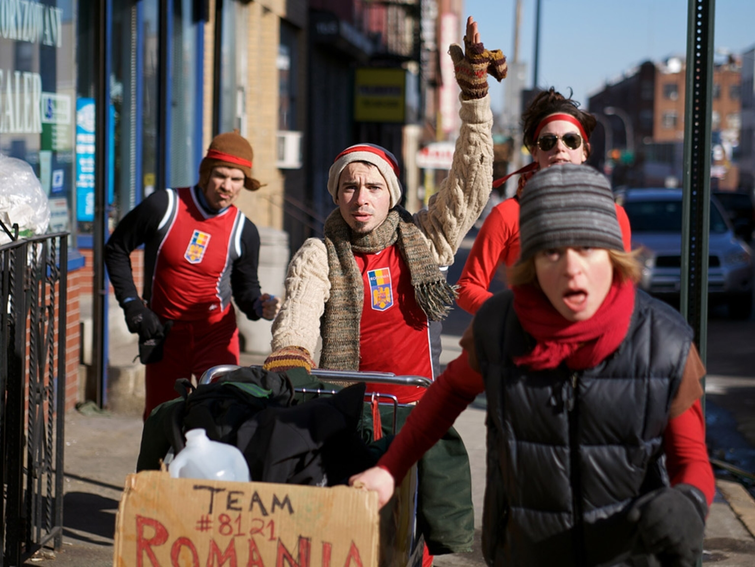 Four people racing with shopping cart down street