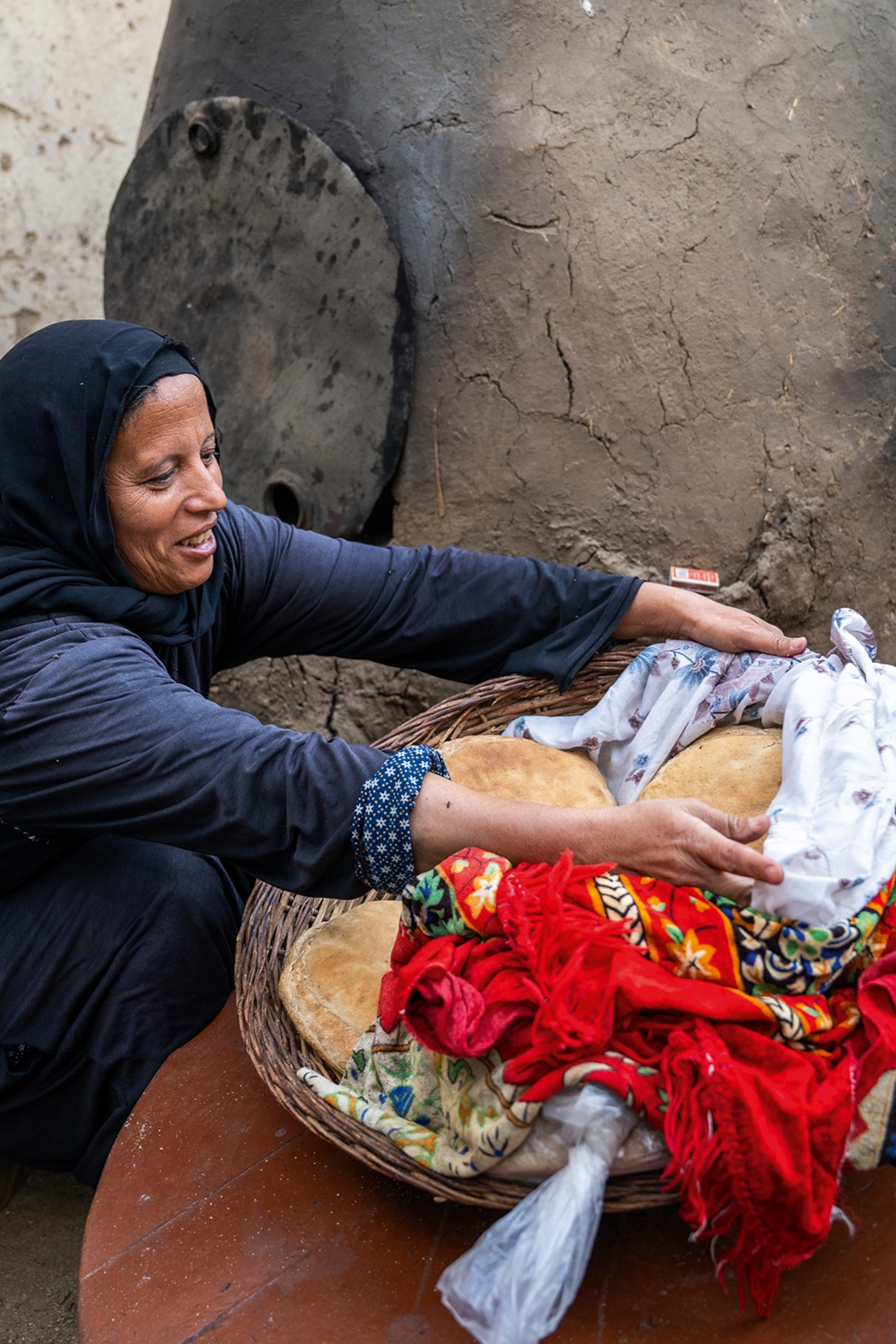 A local woman in Egypt presenting fresh bread in a basket on the floor.