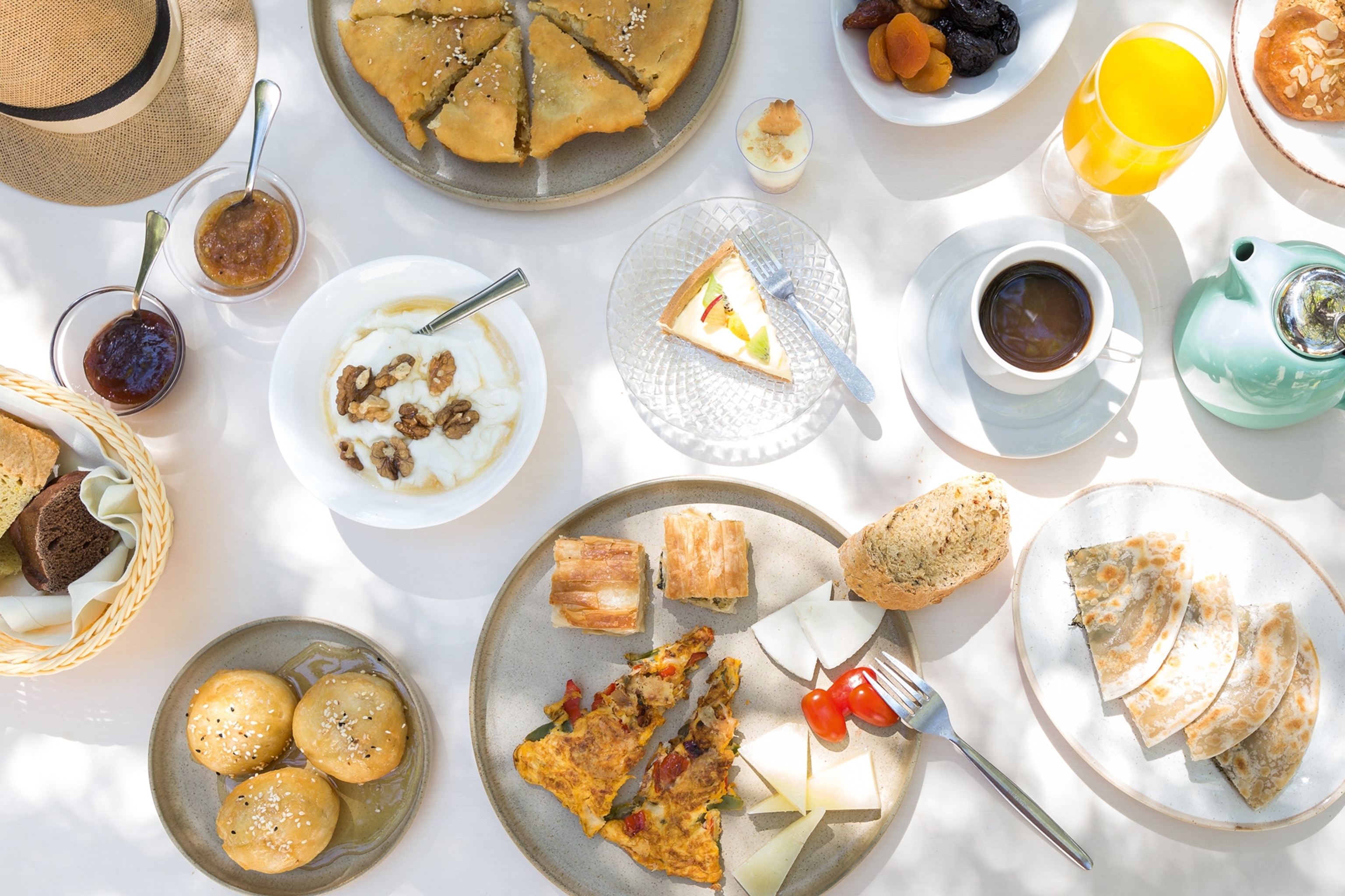 A table scape of different plates of cheese, dried fruits, bread, olive oil and glasses of juice.