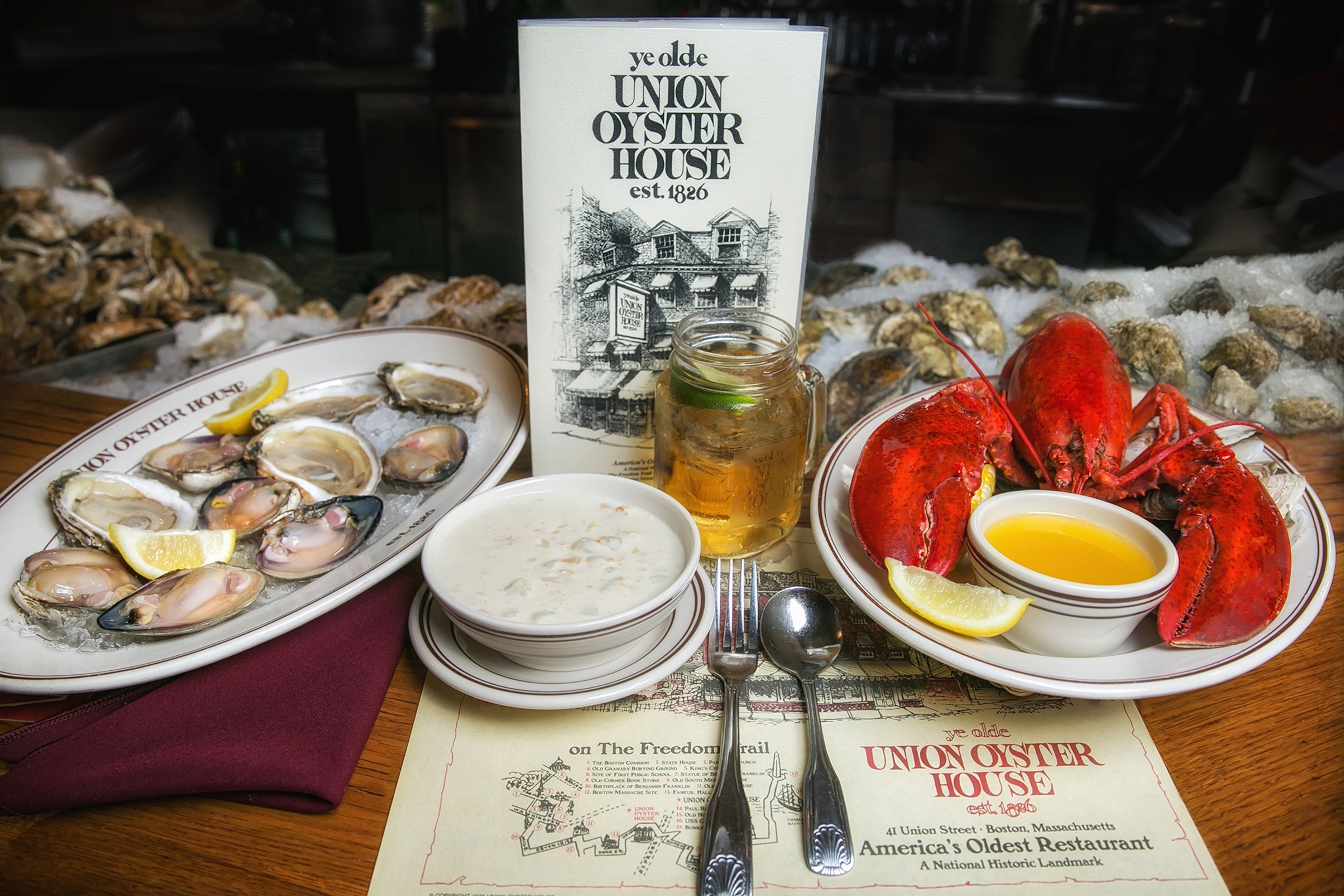 A restaurant spread with a whole lobster, a bowl of clam chowder and a side of oysters.