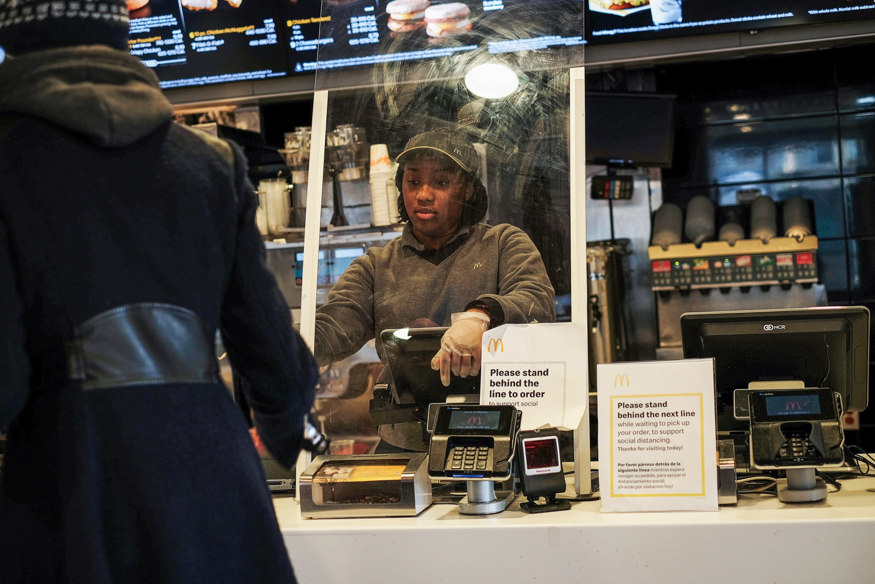 a woman standing behind a glass protector at a McDonalds checkout