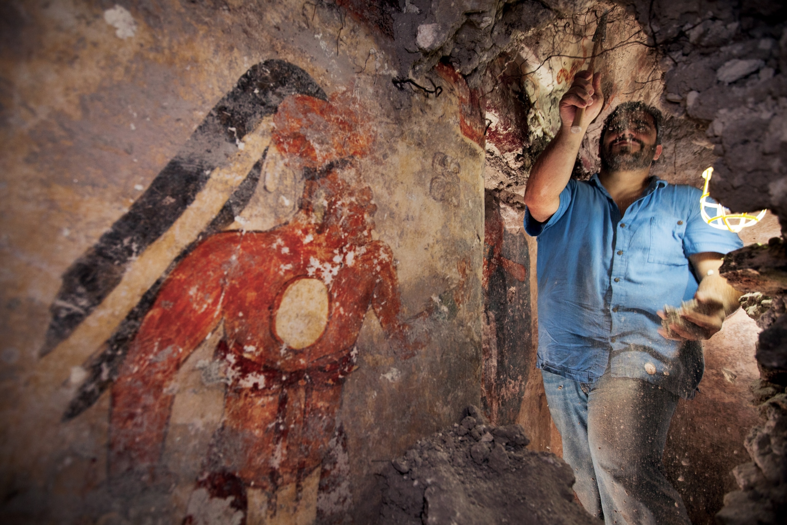 An archeologist scrapes debris near a Maya mural painting.