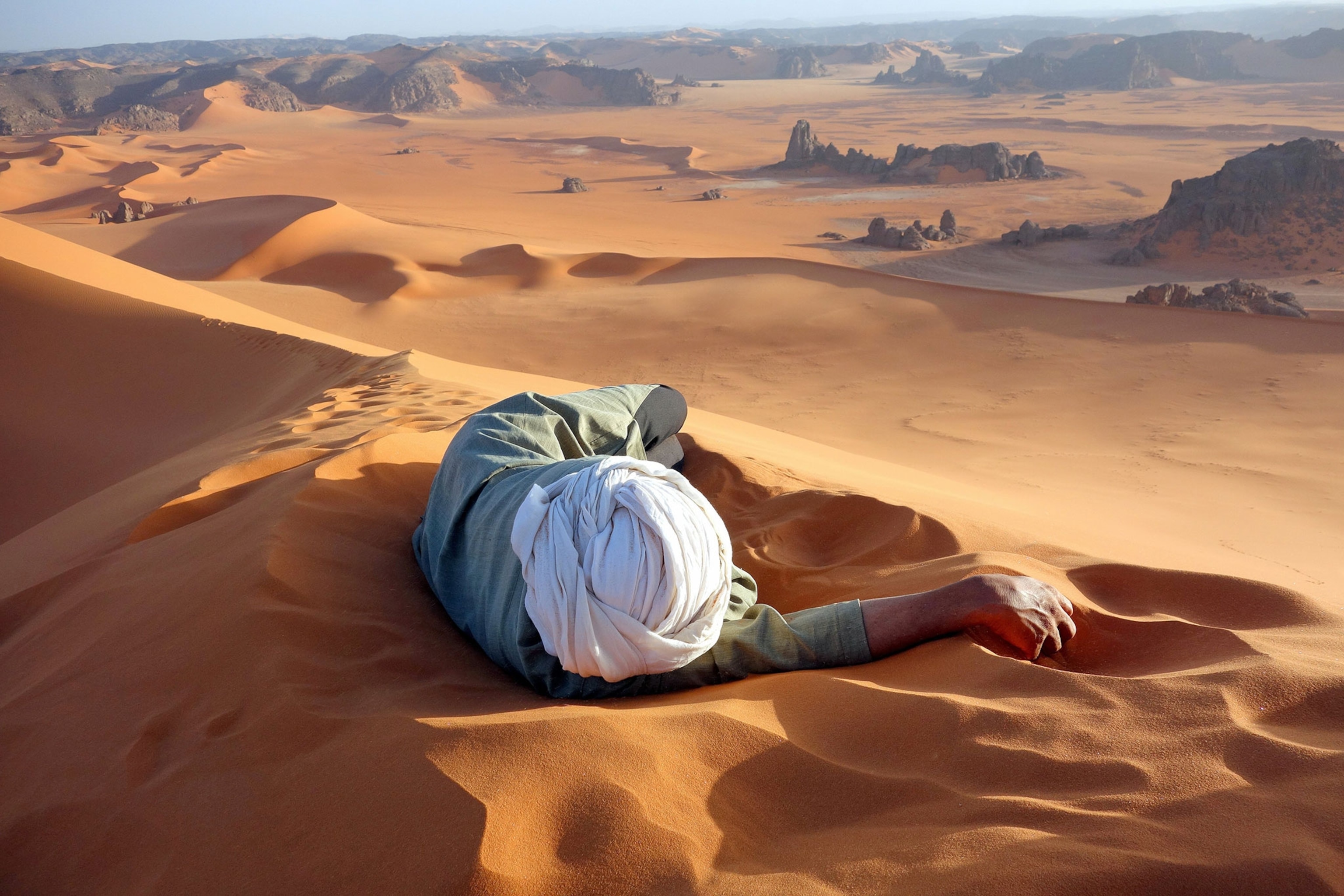 Moussa Macher, a Tuareg guide, rests at the summit of Tin-Merzouga, the largest dune (or erg) in the Tadrat region of the Sahara desert in southern Algeria, while waiting for his group to finish their climb to the top.