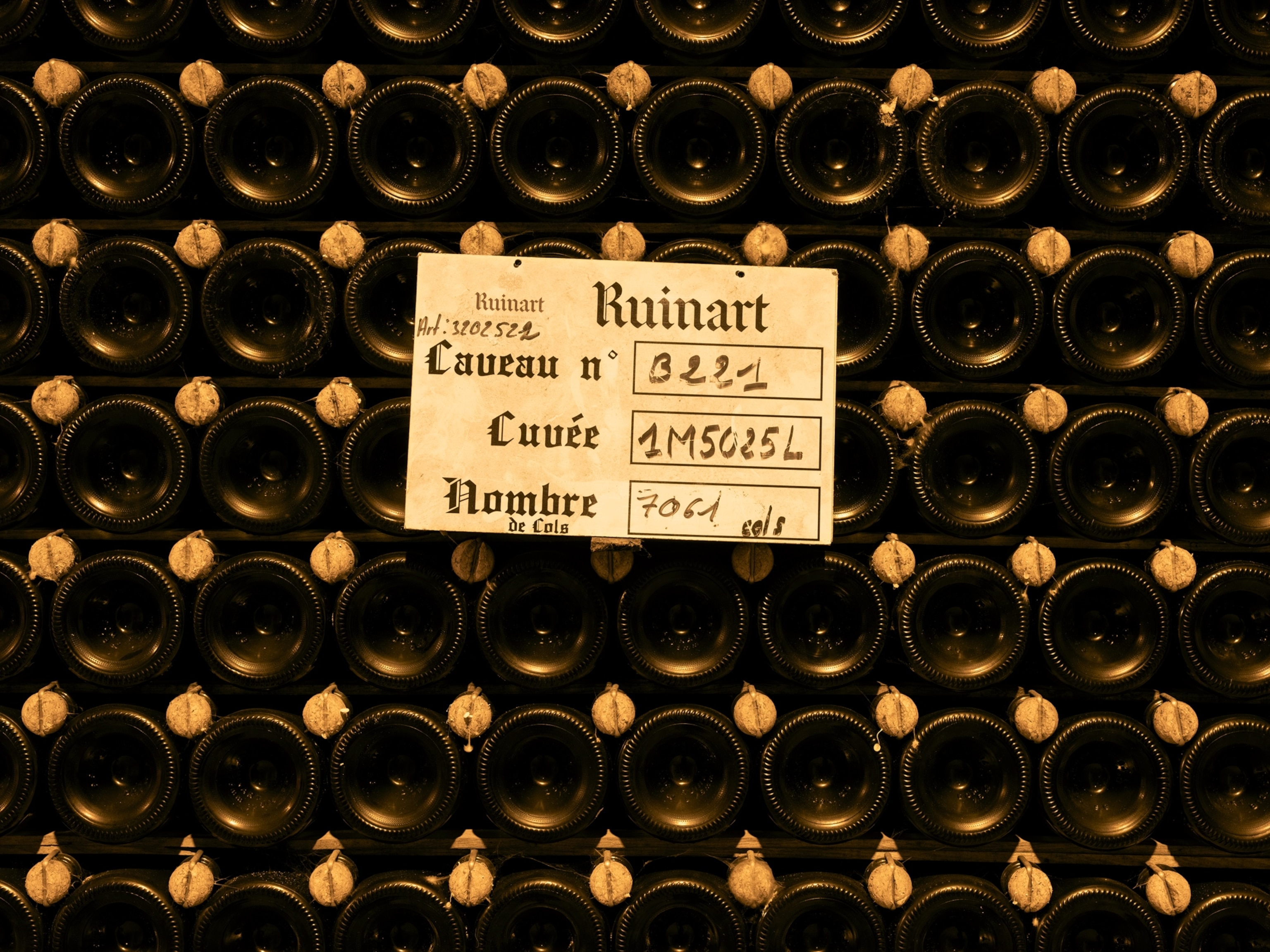  storage label is attached to stacks of wine bottles in the Crayères cellar at Ruinart Champagne, showing rows of bottles resting inside the historic former chalk quarries in Reims, France.