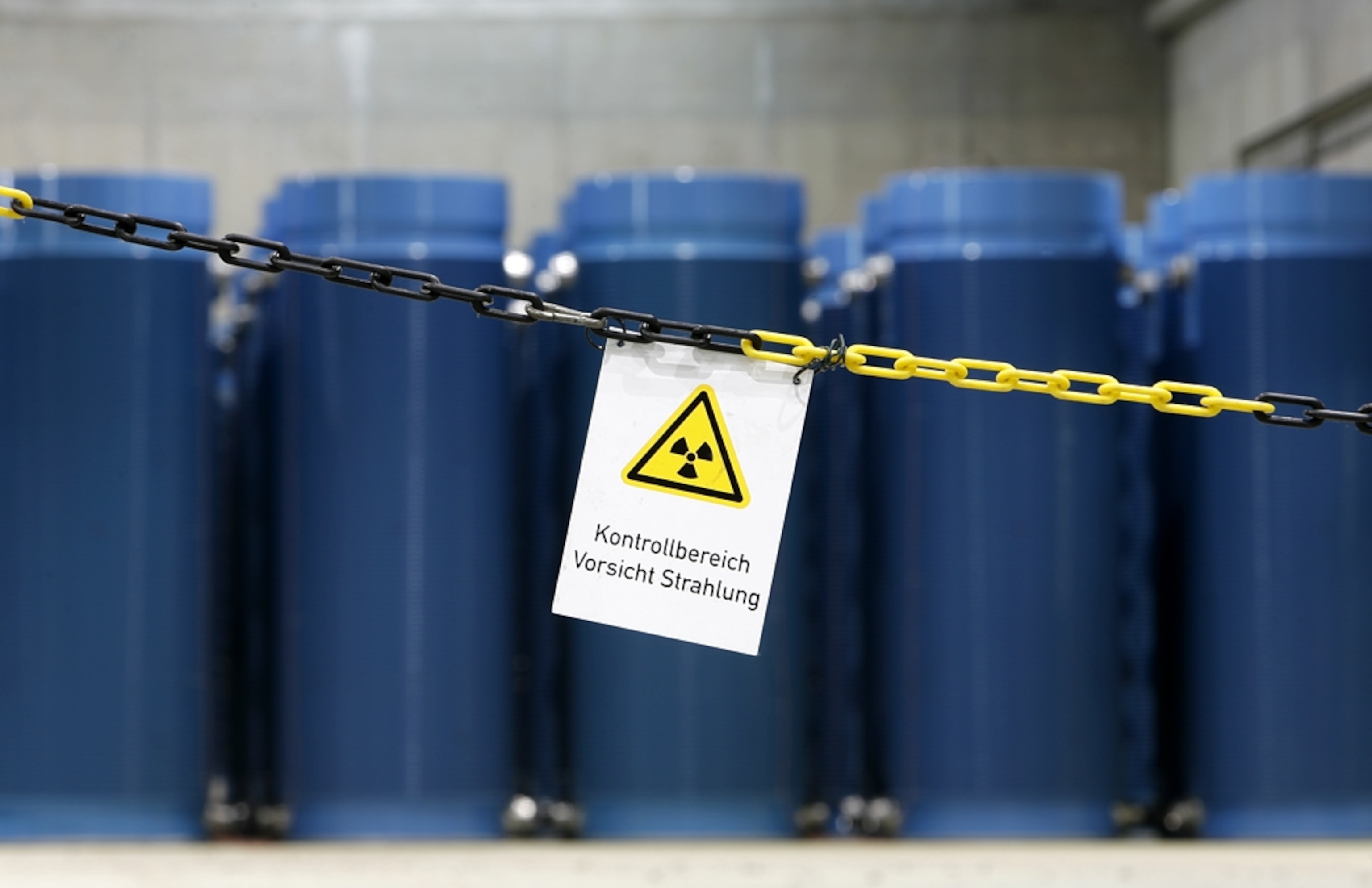 A row of blue canisters, containing nuclear waste, sits behind a chain and a warning sign (picture)