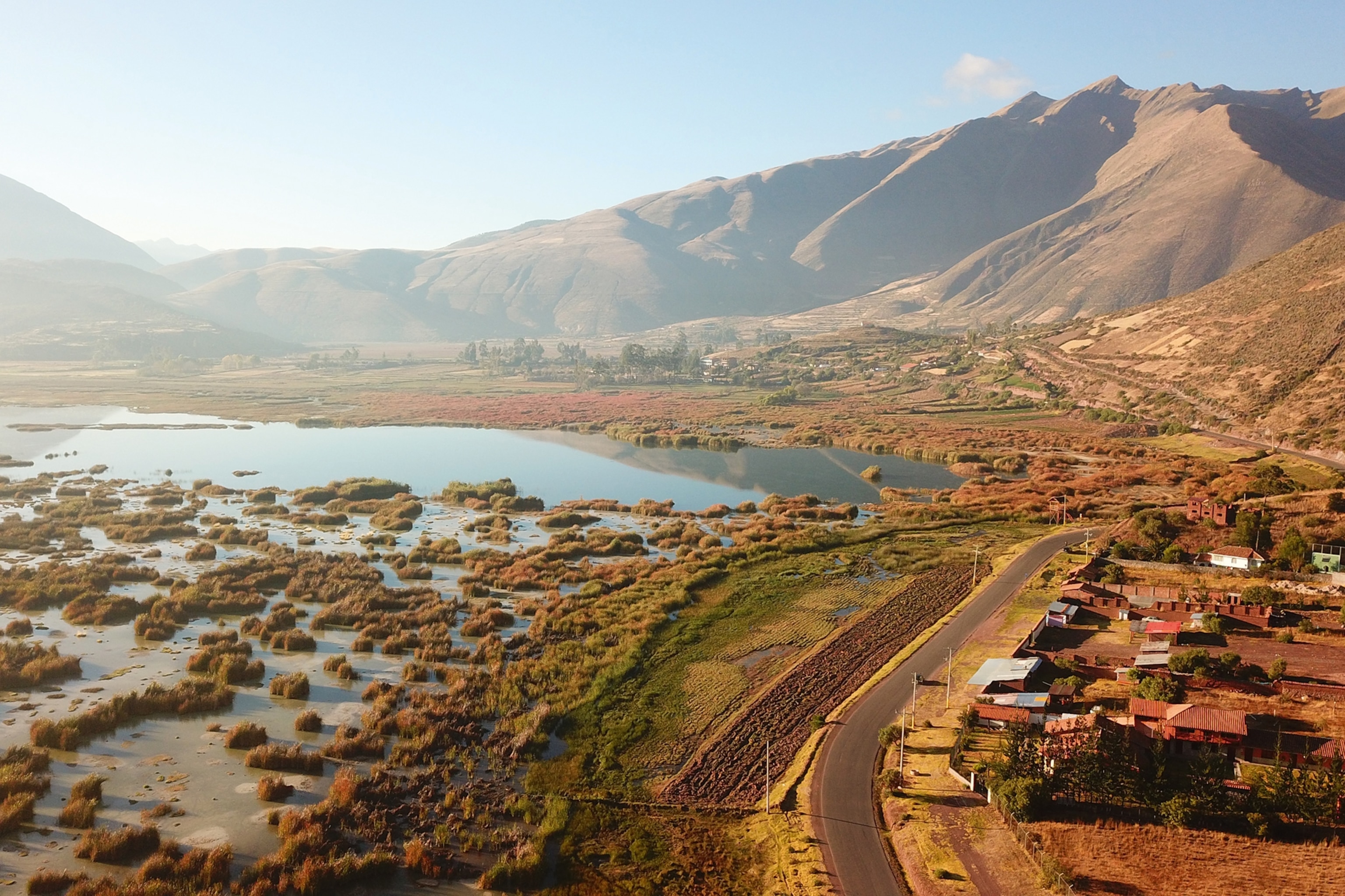An aerial shot of a clear lake eating into the edge of a mountain pass with only a road separating the two.