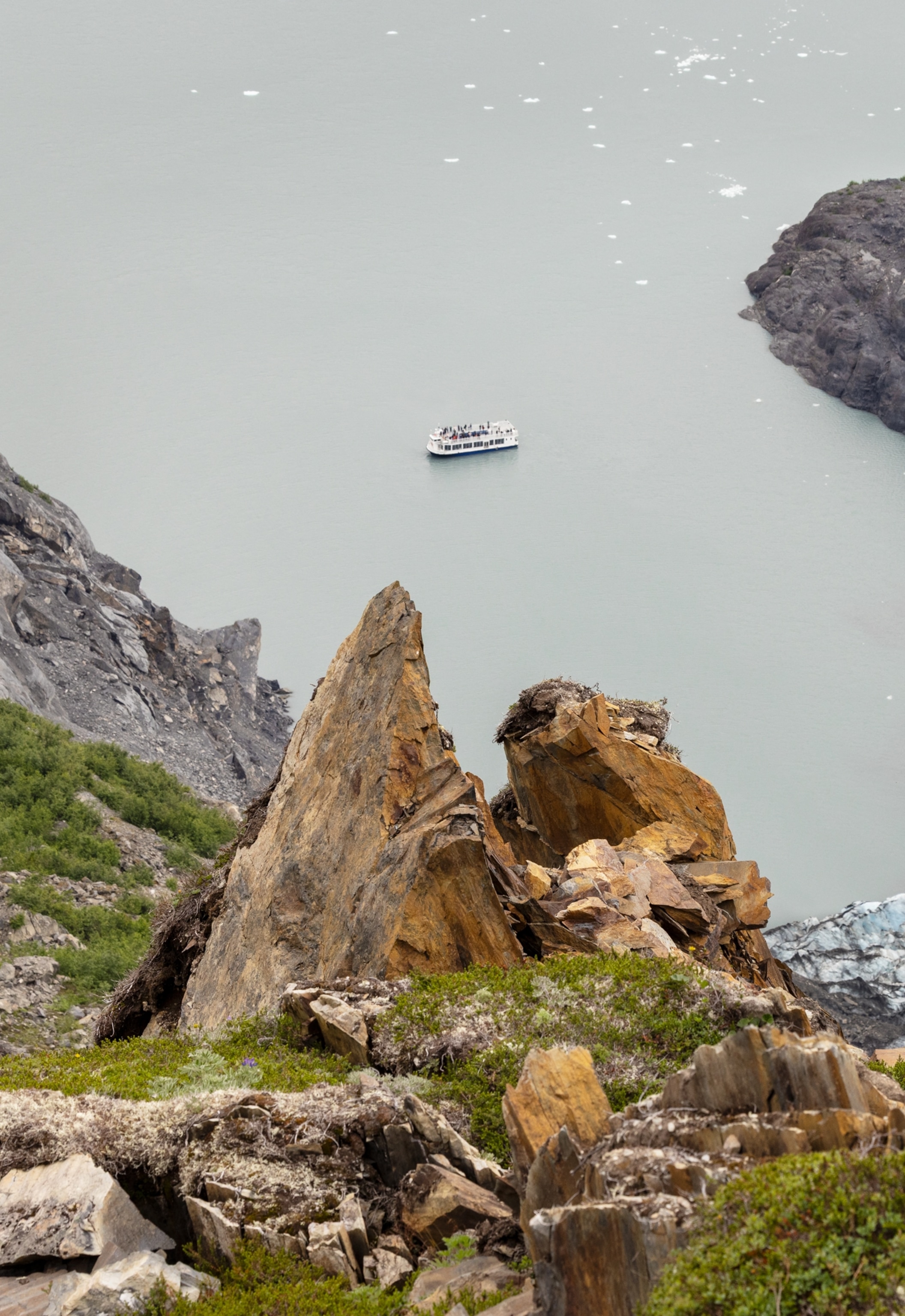 A white boat floats on pale gray water, seen from above between steep rocky cliffs.