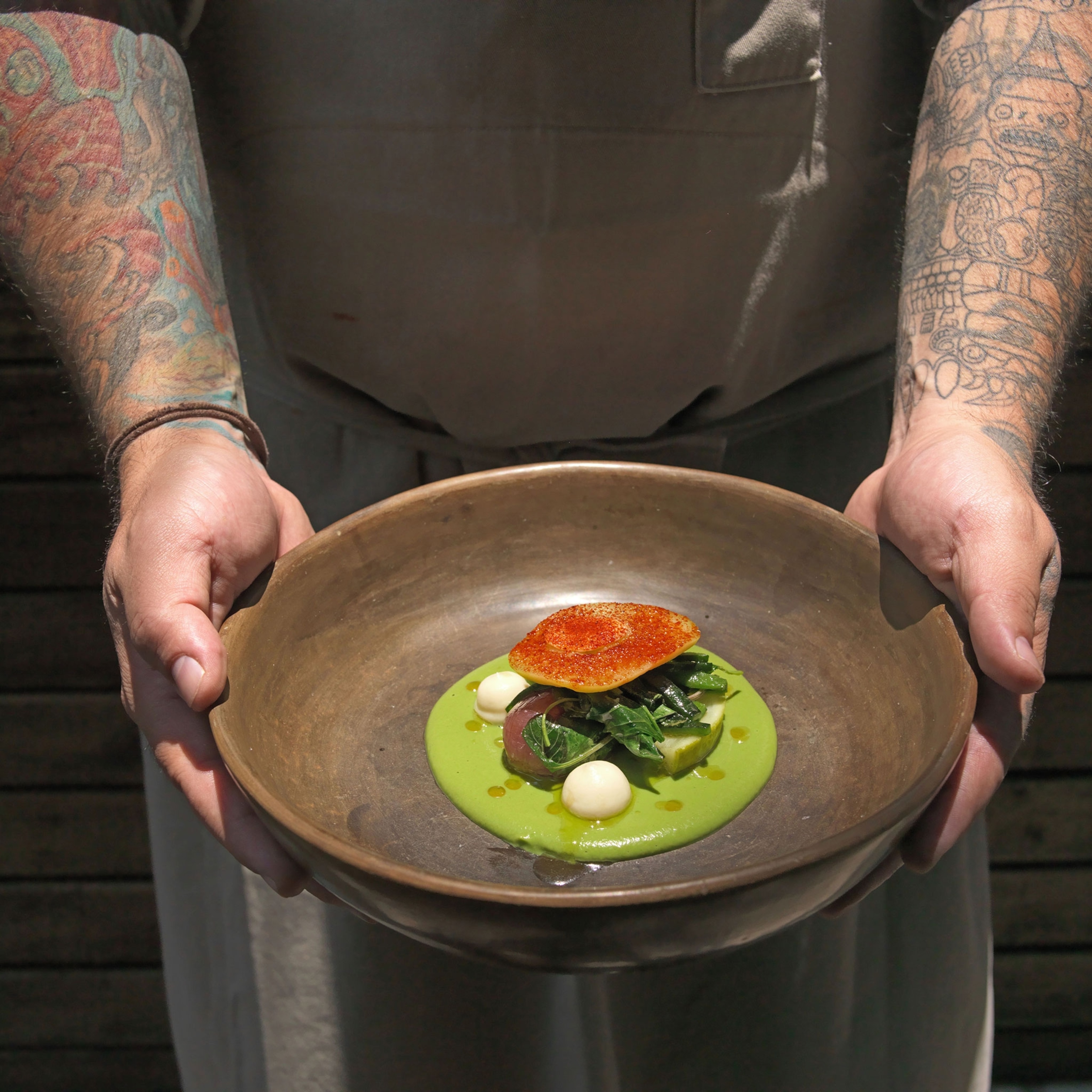 Hands holding a dark colored bowl. with a green sauce.