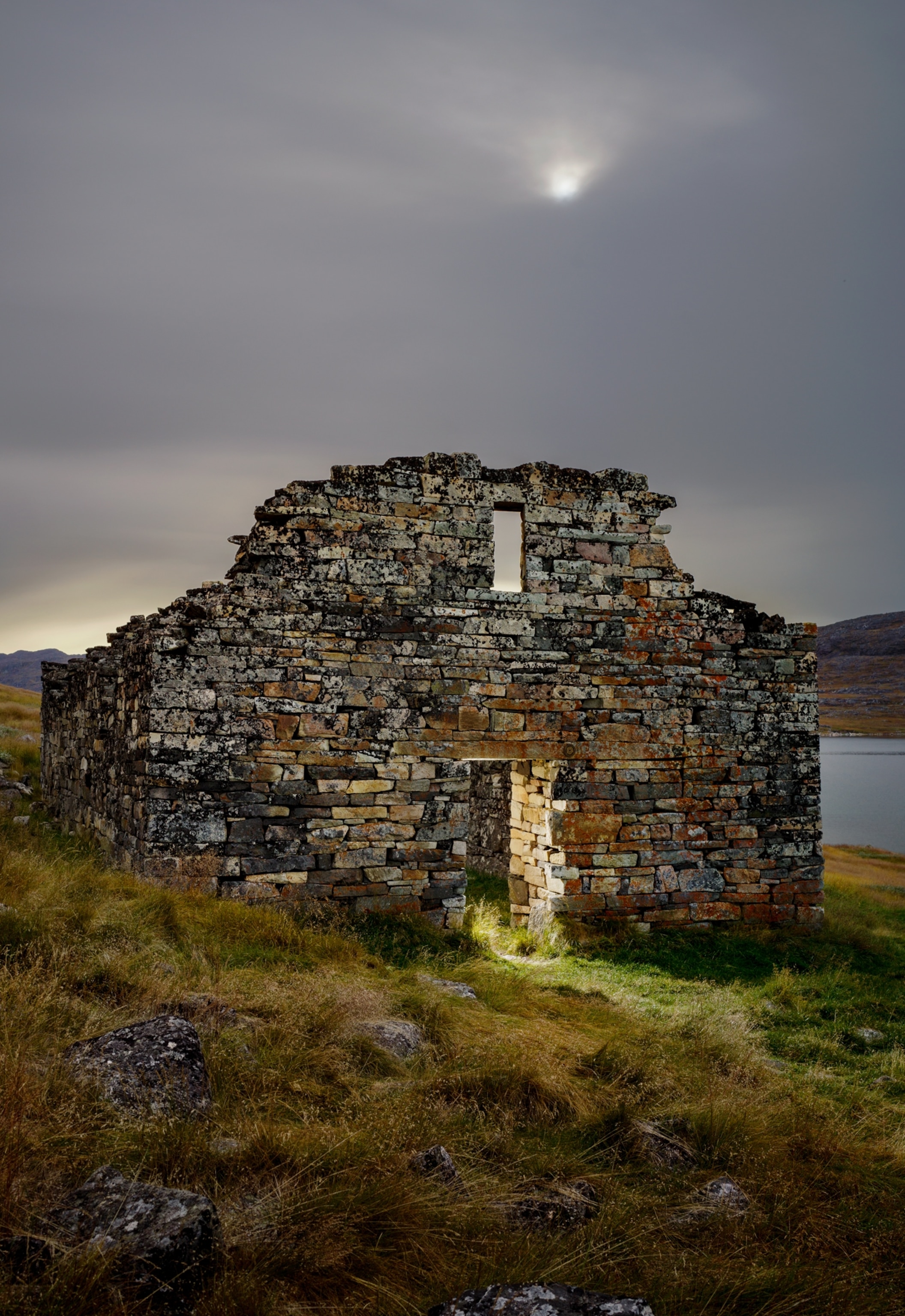 Ruin with doorway and window lit from behind against heavy gray sky.