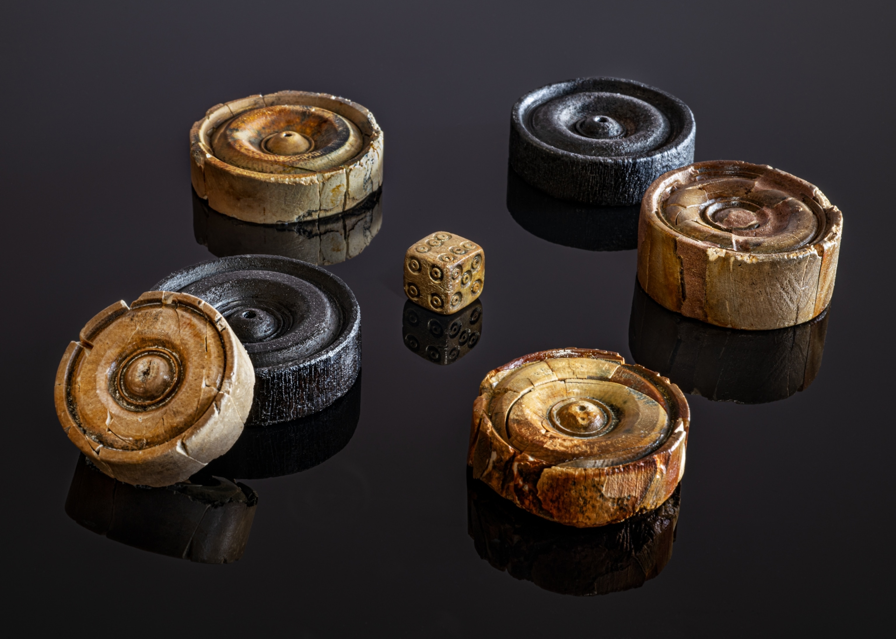 Six circular game pieces resembling checkers pieces and a carved six-sided die.