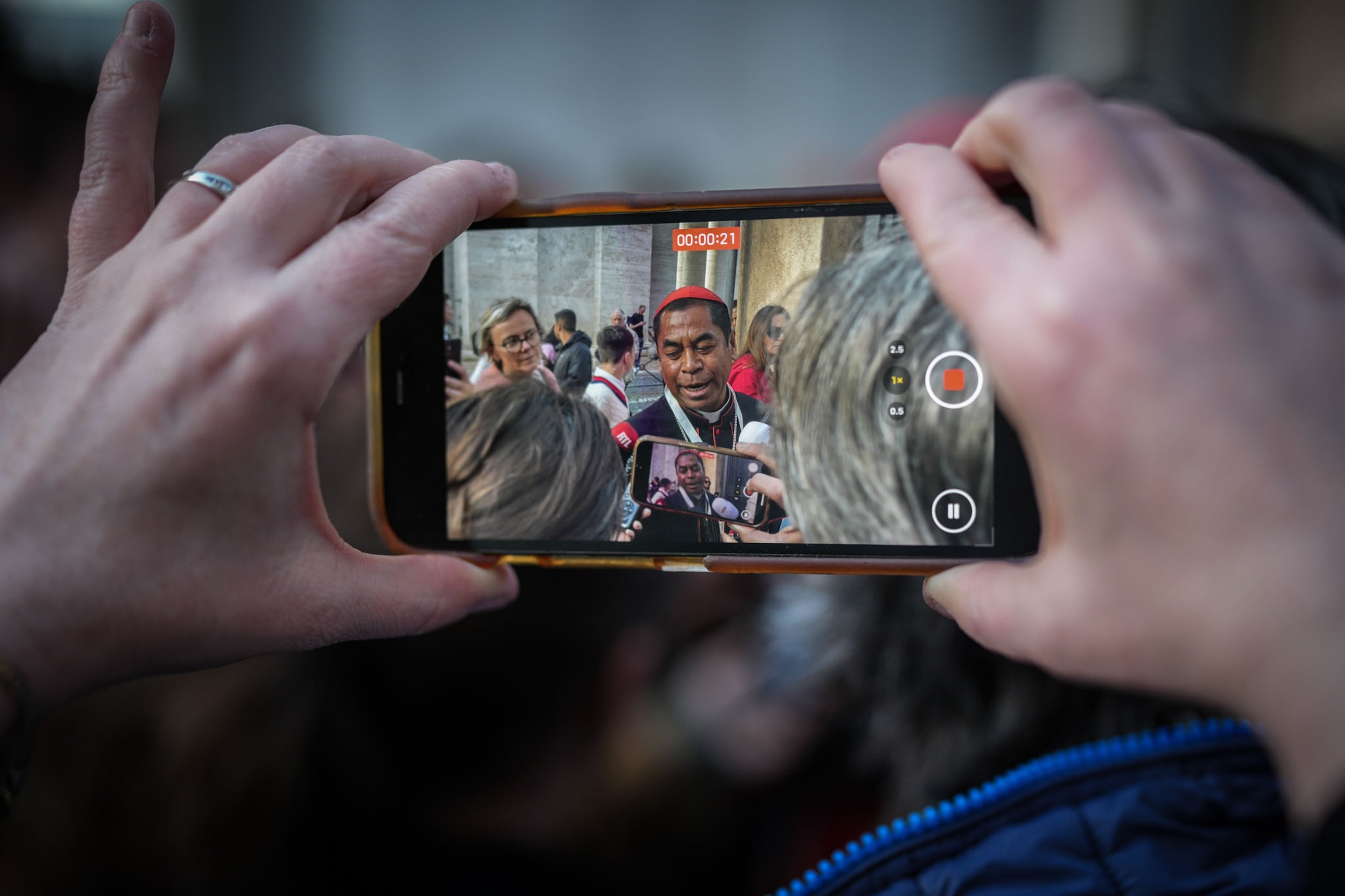 A phone screen recording a video shows the screen of another phone's video recording of a man speaking.