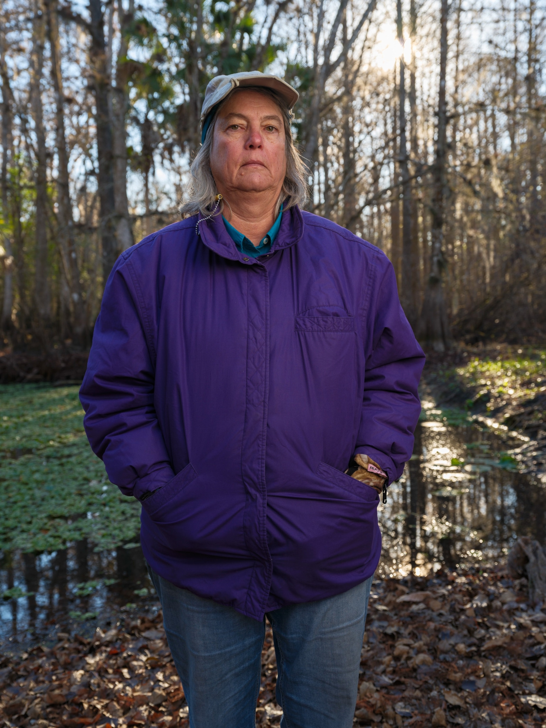 Captain Erika Ritter in a purple jacket and cap standing with hands in pockets amidst a serene, sunlit woodland.