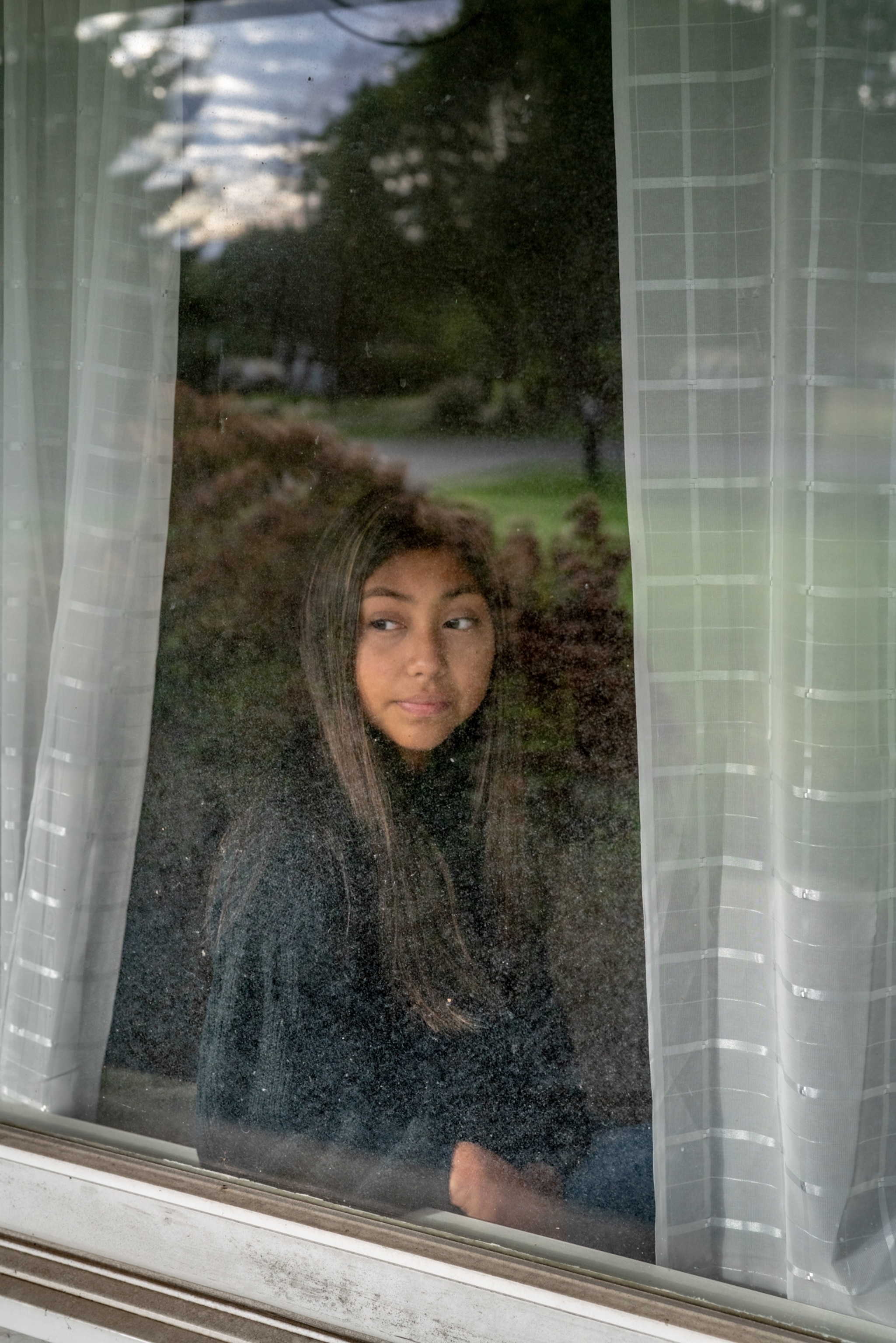 a girl sits in her home in Michigan, looking out the window