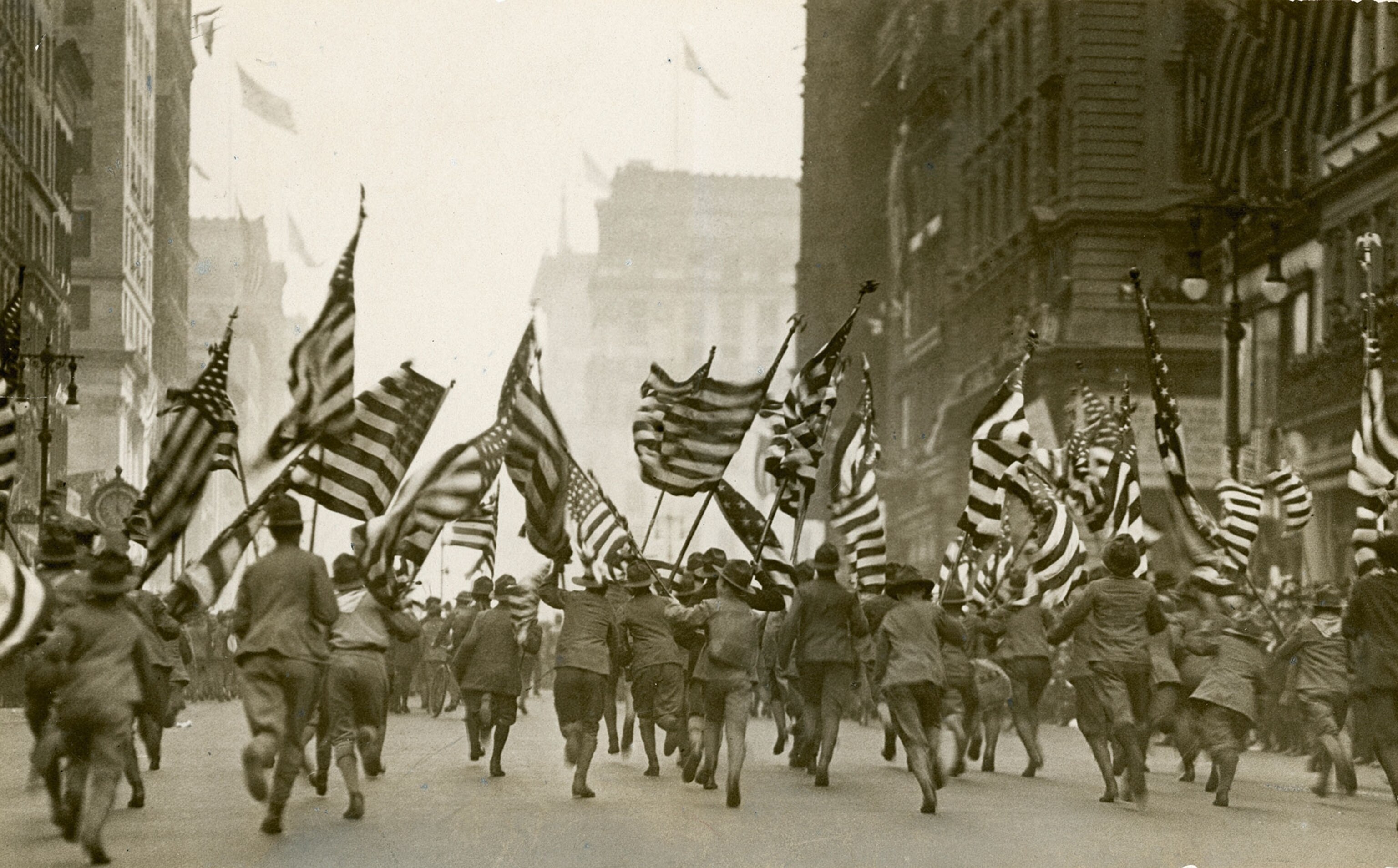 group of Boy Scouts waving American flags while racing through a city street
