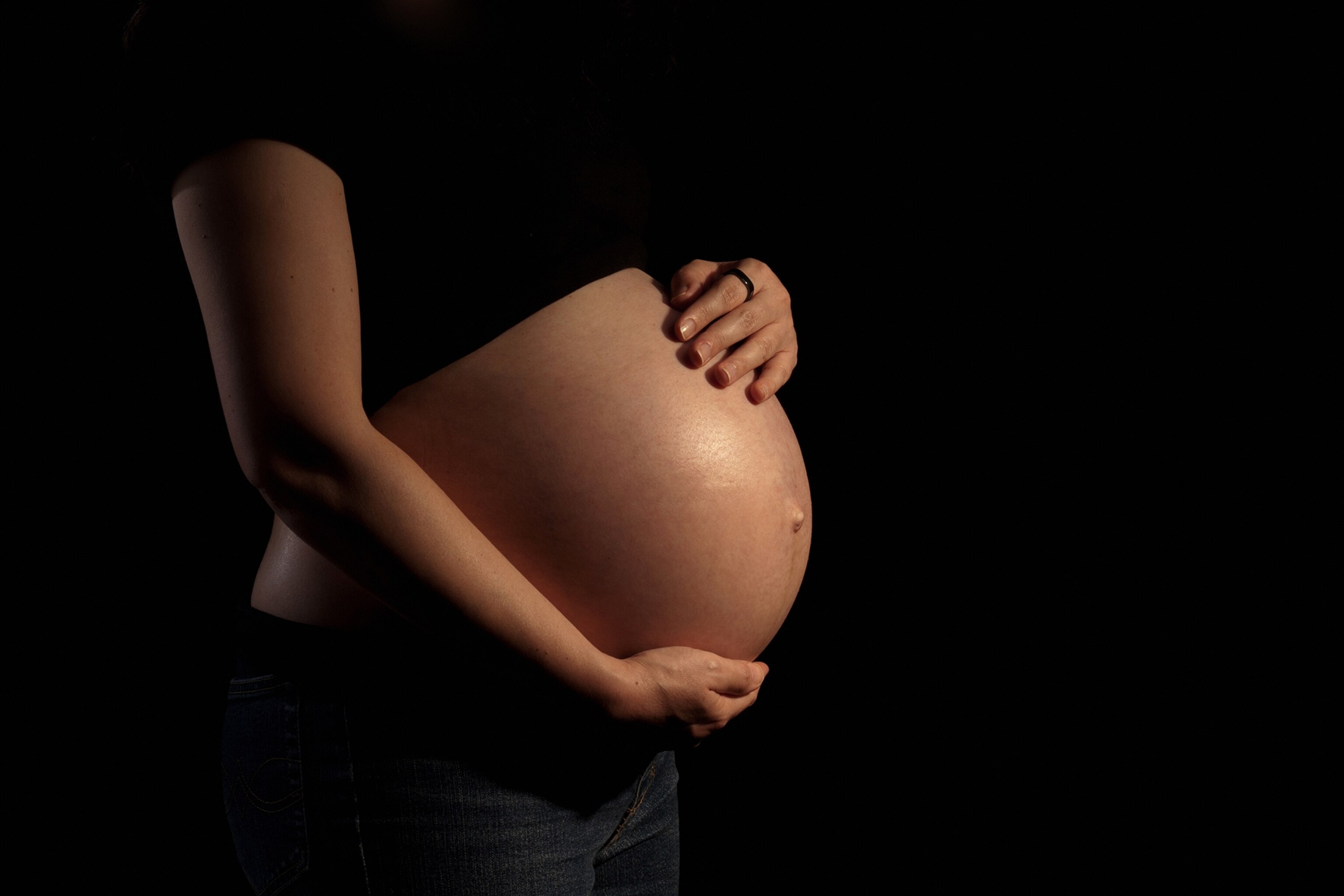 A pregnant woman takes a photograph on a black background.