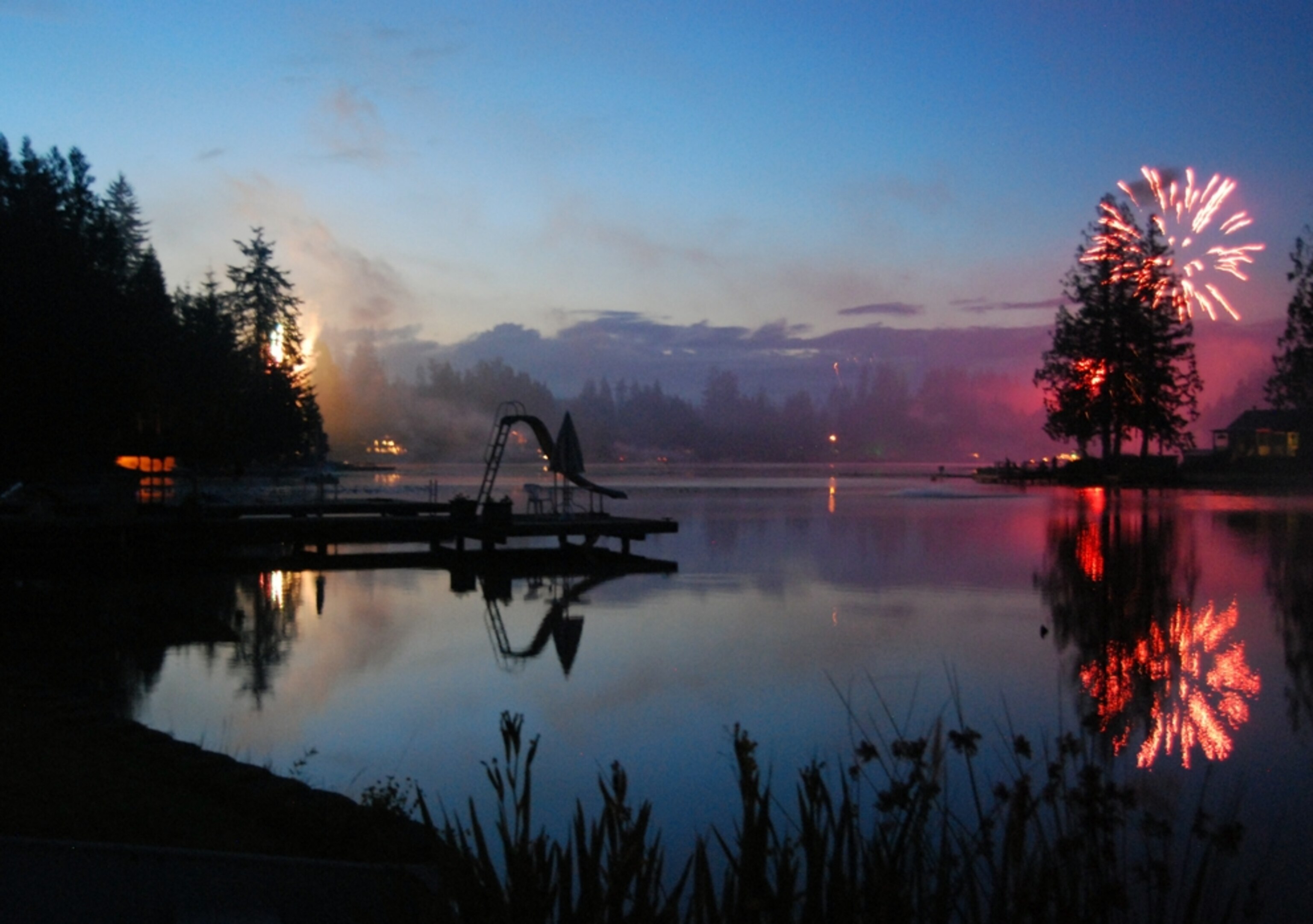 A lake reflects the night sky's glow on the Fourth of July at Lake Roesiger, Washington