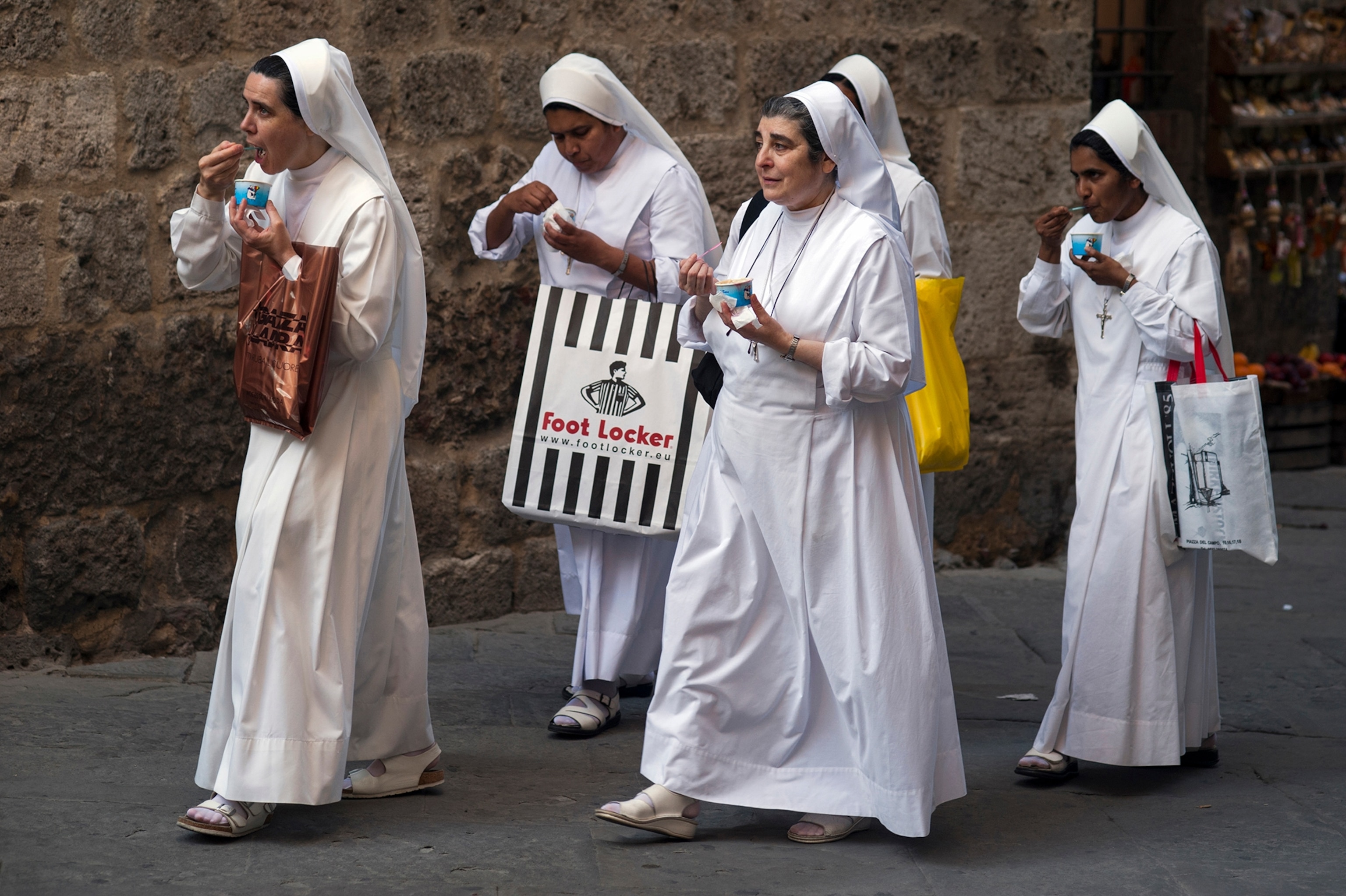 A group of nuns walk down the street eating ice cream.