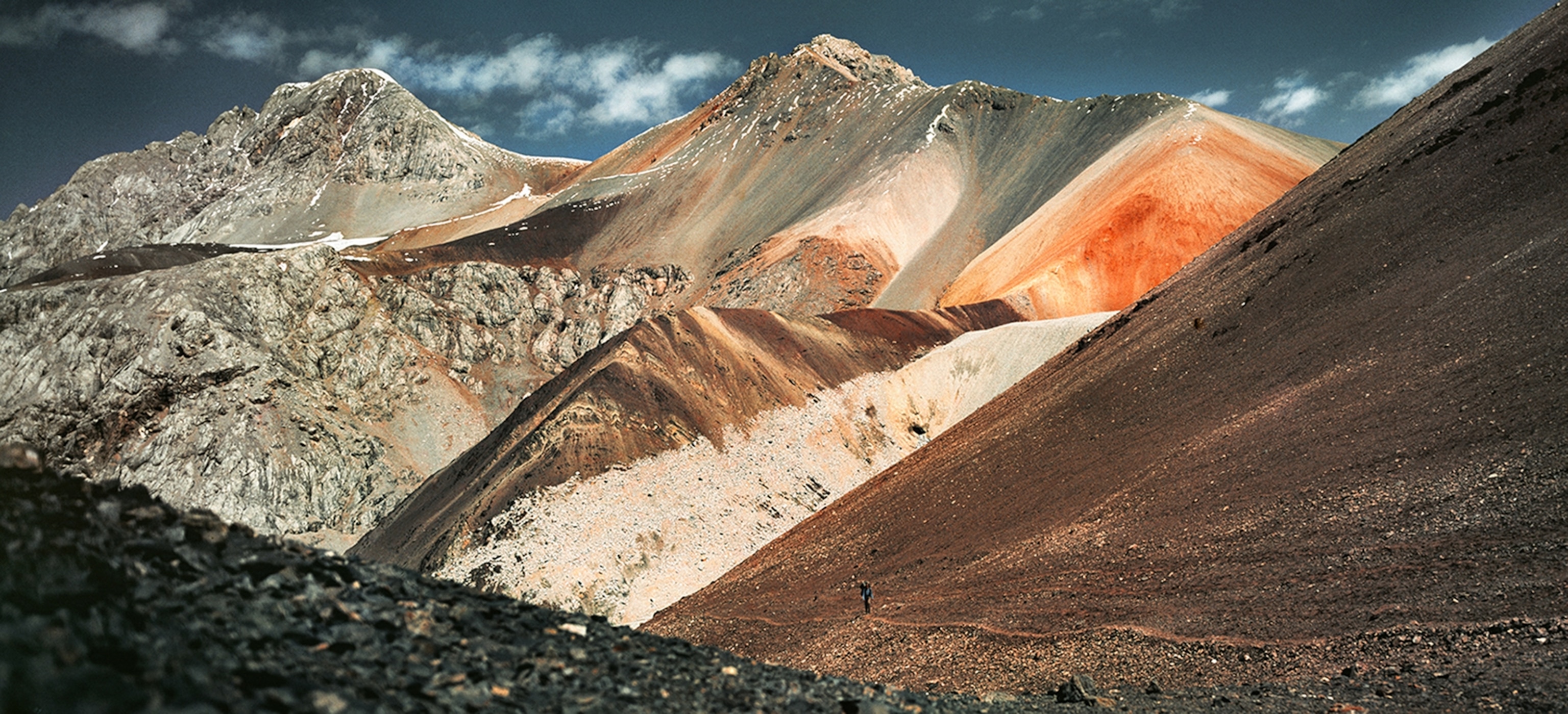 Landscape of a mountain range with brown, grey, green, and orange stone creating a variety of color.