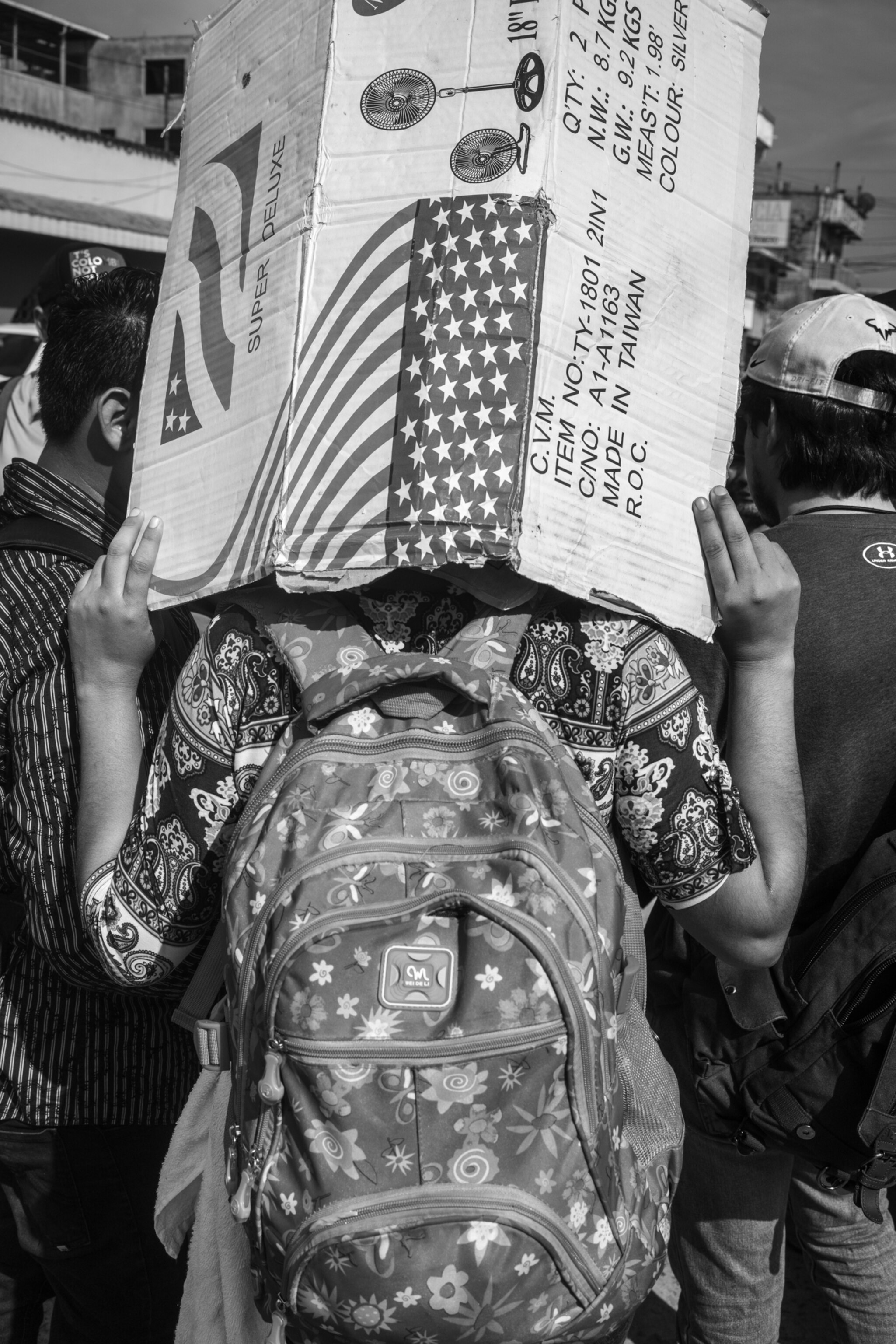 the back of a man wearing a backpack holding a cardboard box over his head