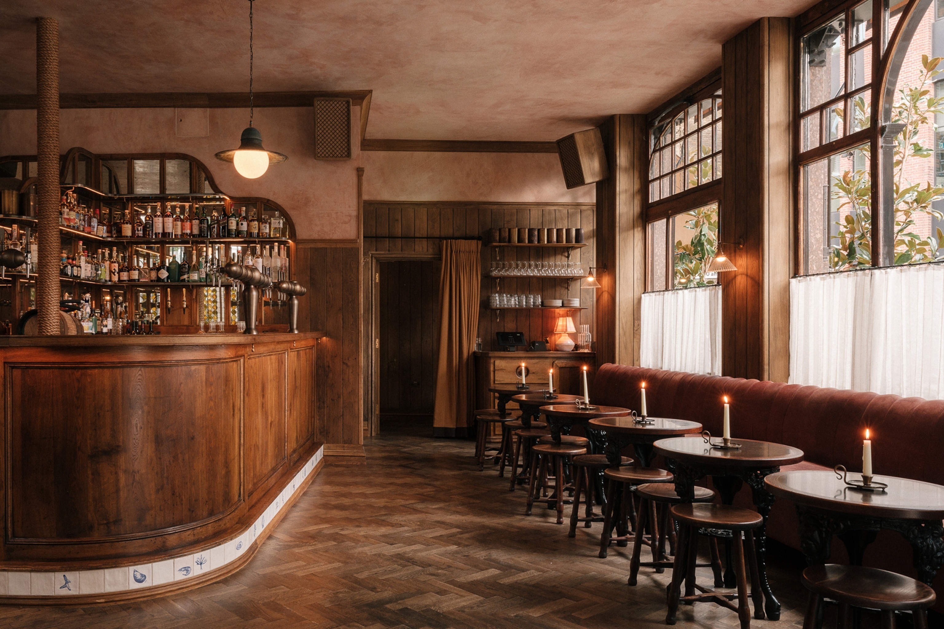 The interiors of a cosy, wood-panelled pub with a curved bar and tables along the window front.