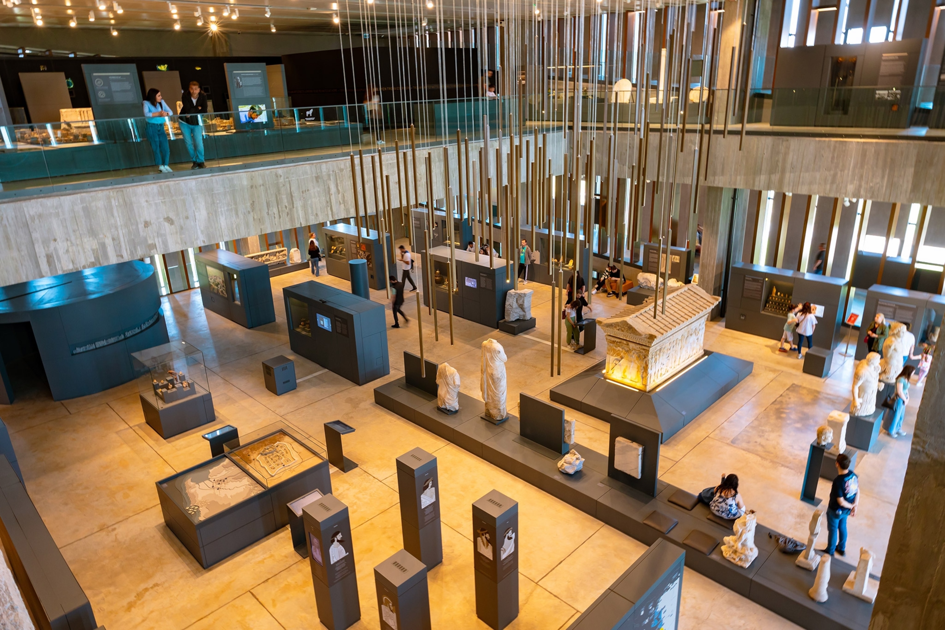 A view from a balcony down into a museum room filled with artifacts and placards and visitors