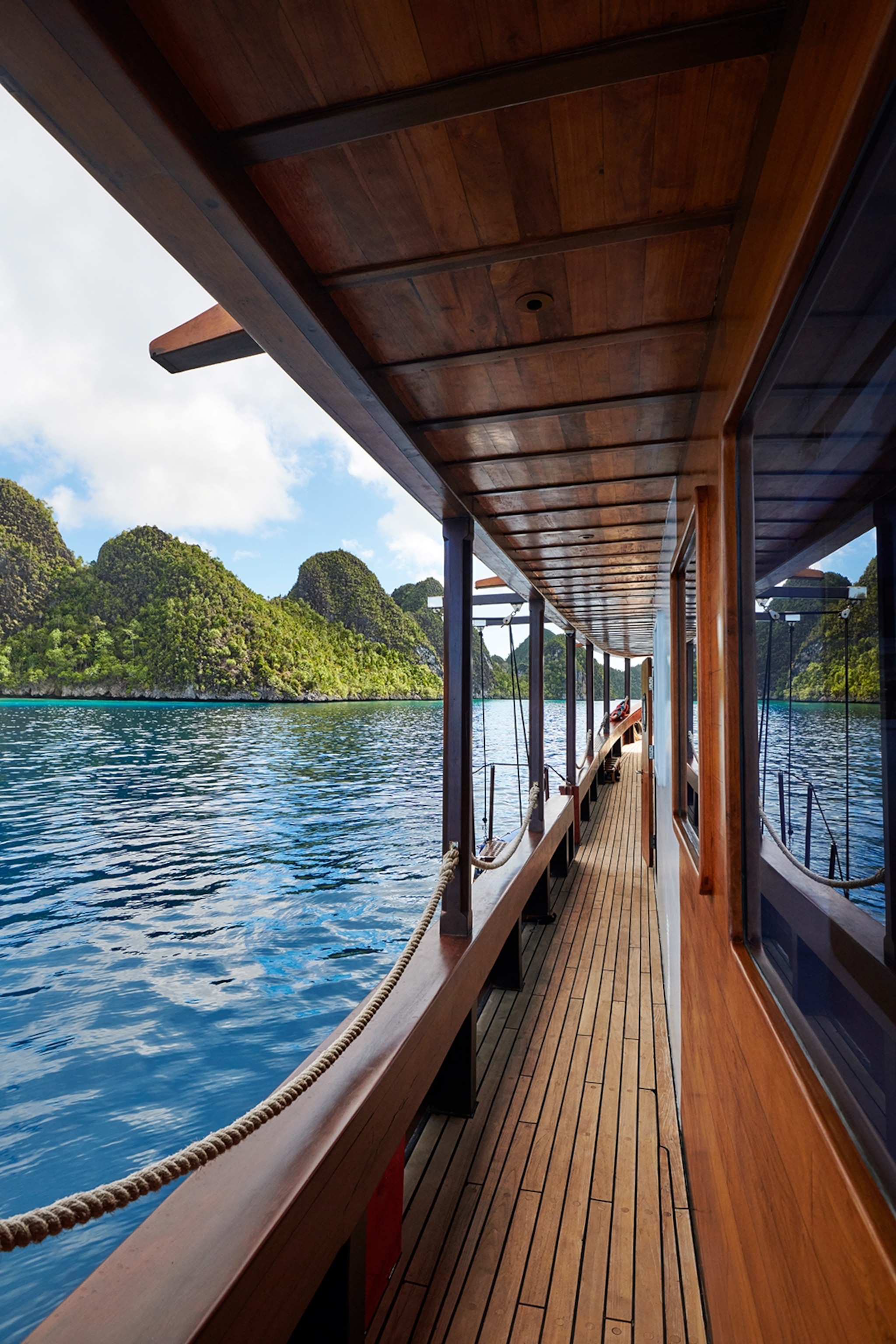 The wooden sidewalk on a low river boat, looking out at islands and clear water.