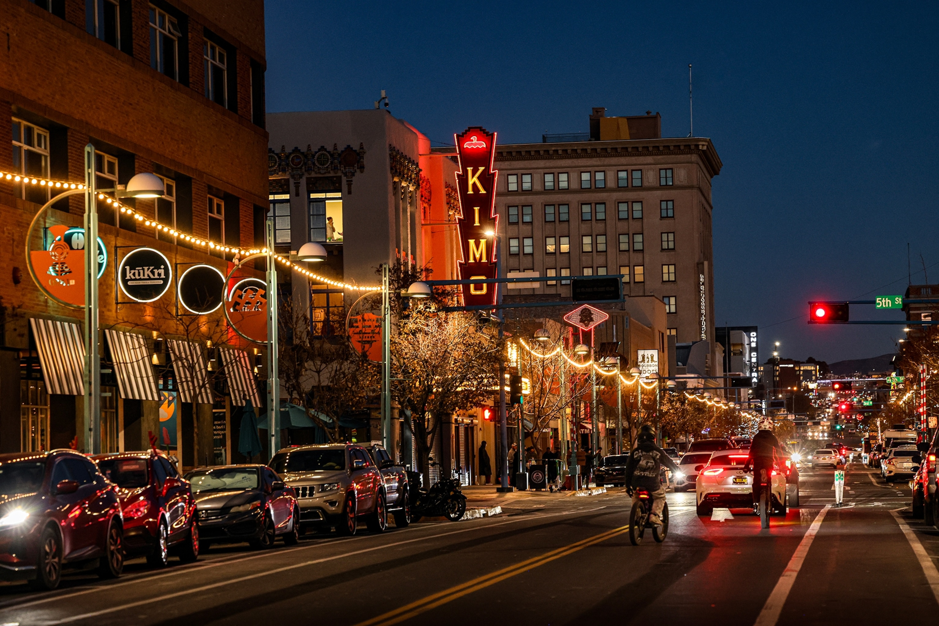 A nighttime shot of a high street with ferry lights hang between lamp posts and shop signs lining the buildings.