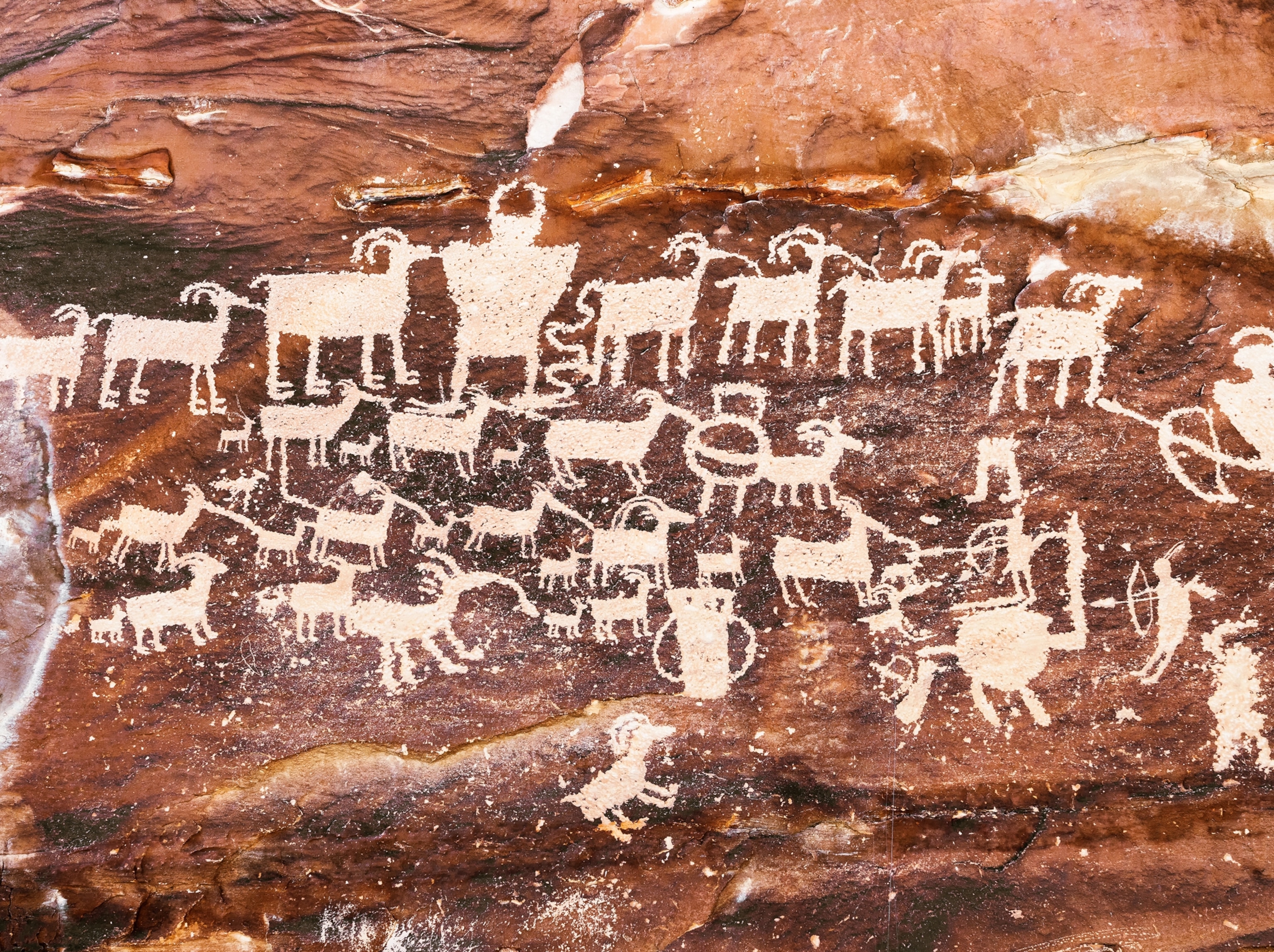 Carvings of people and animals are seen on a red cave wall