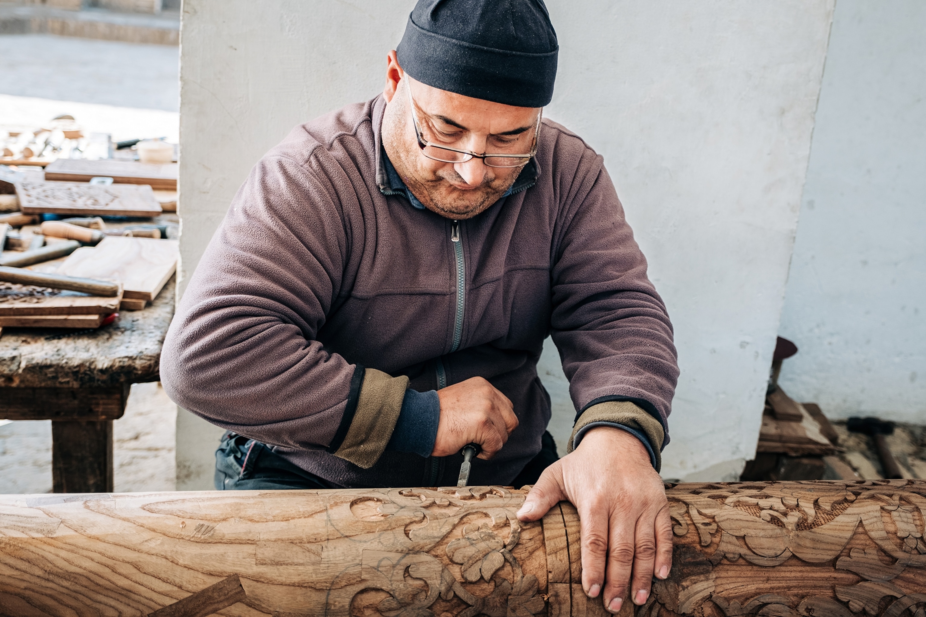 A local man concentrating on carving a wood column with decorative features.