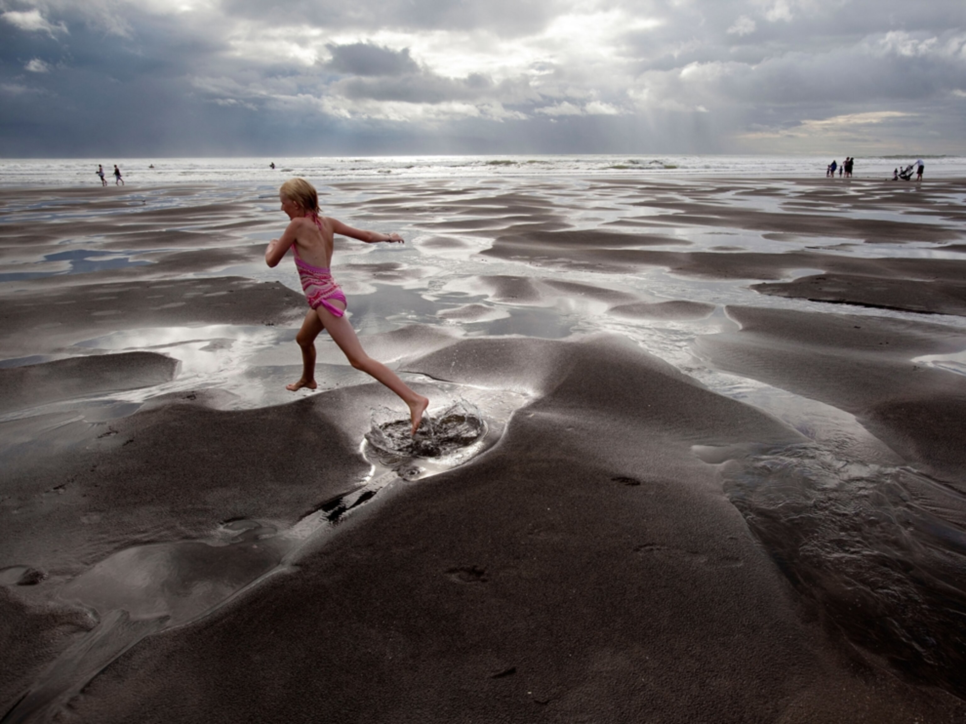 a young girl jumping over puddles at low tide on Piha Beach, Auckland, New Zealand.