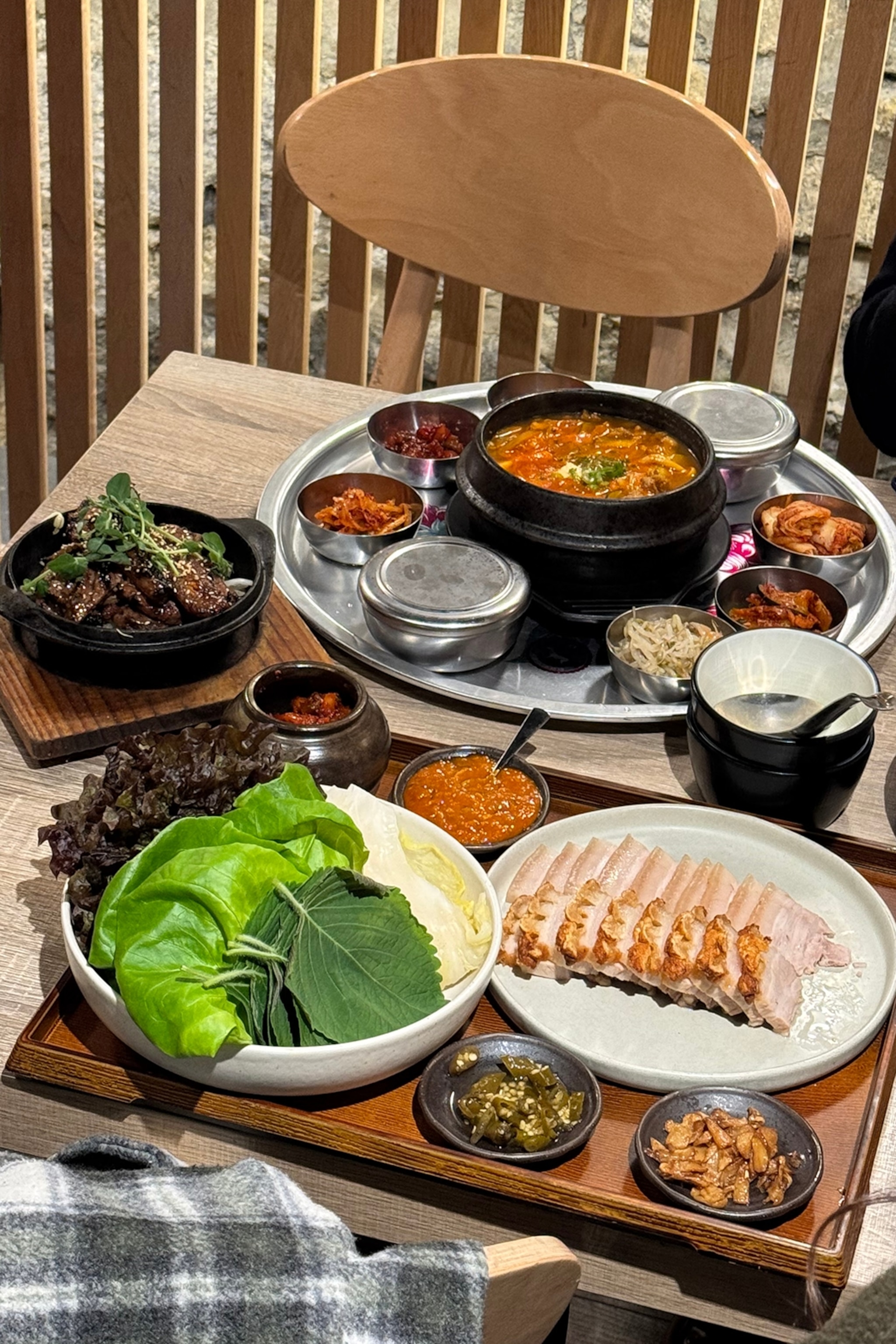 A spread of different dishes in restaurant, including a bean and tofu stew and a platter of boiled and crispy pork belly.