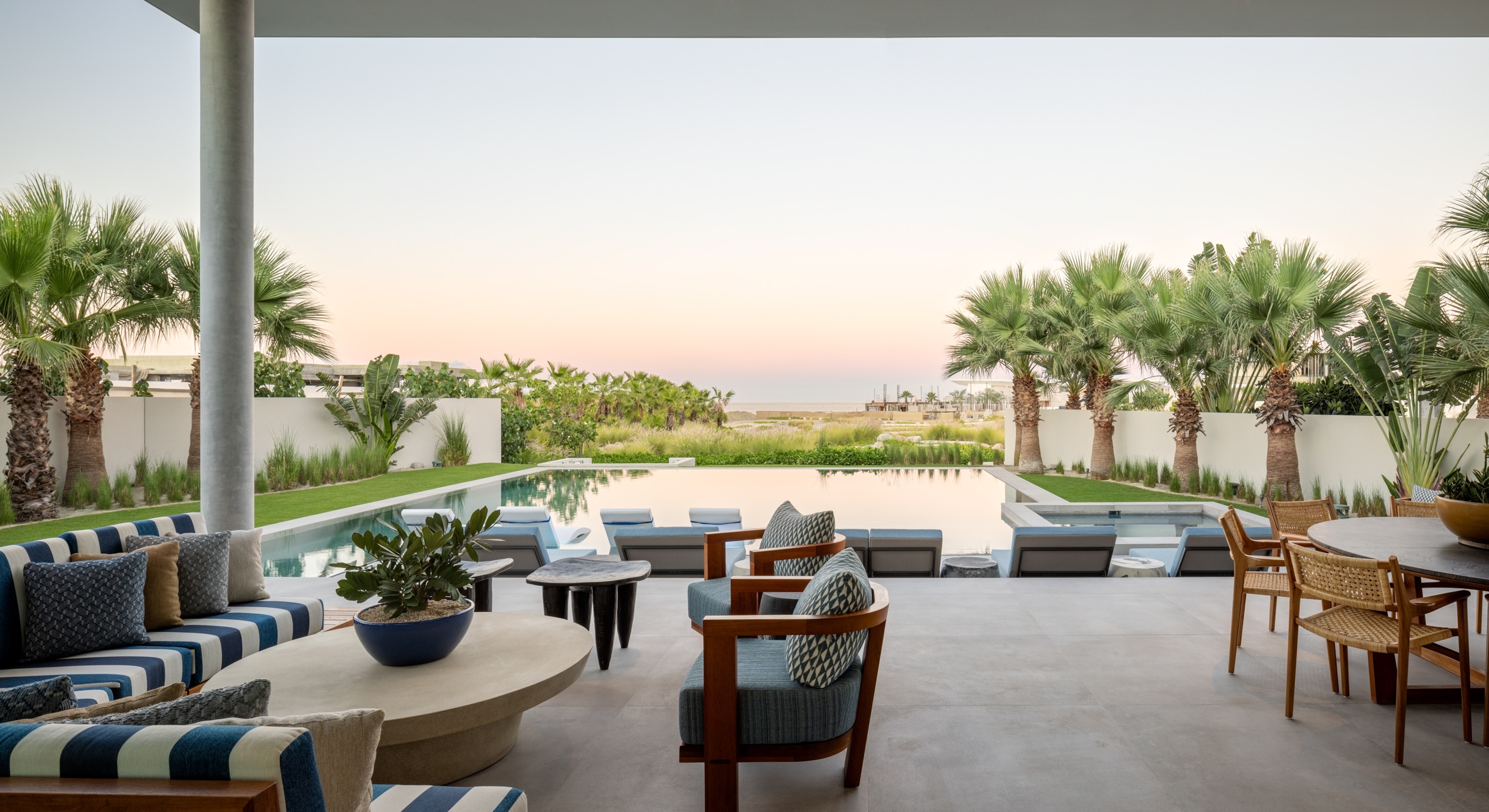 chairs on a concrete deck looking out to a pool and the ocean with palm trees in the yard