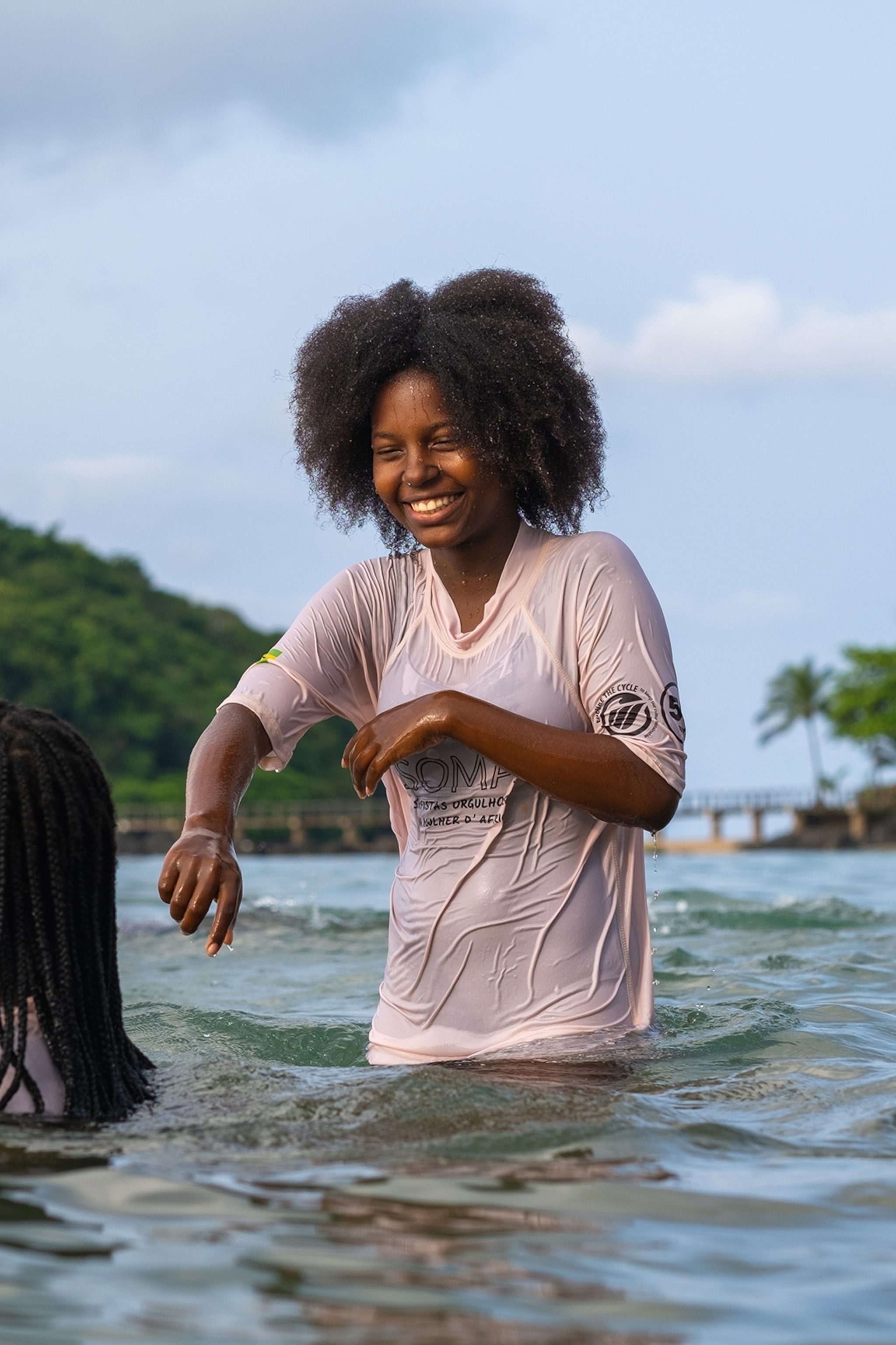 A young girl wearing a long t-shirt, playing in the ocean with her friends.